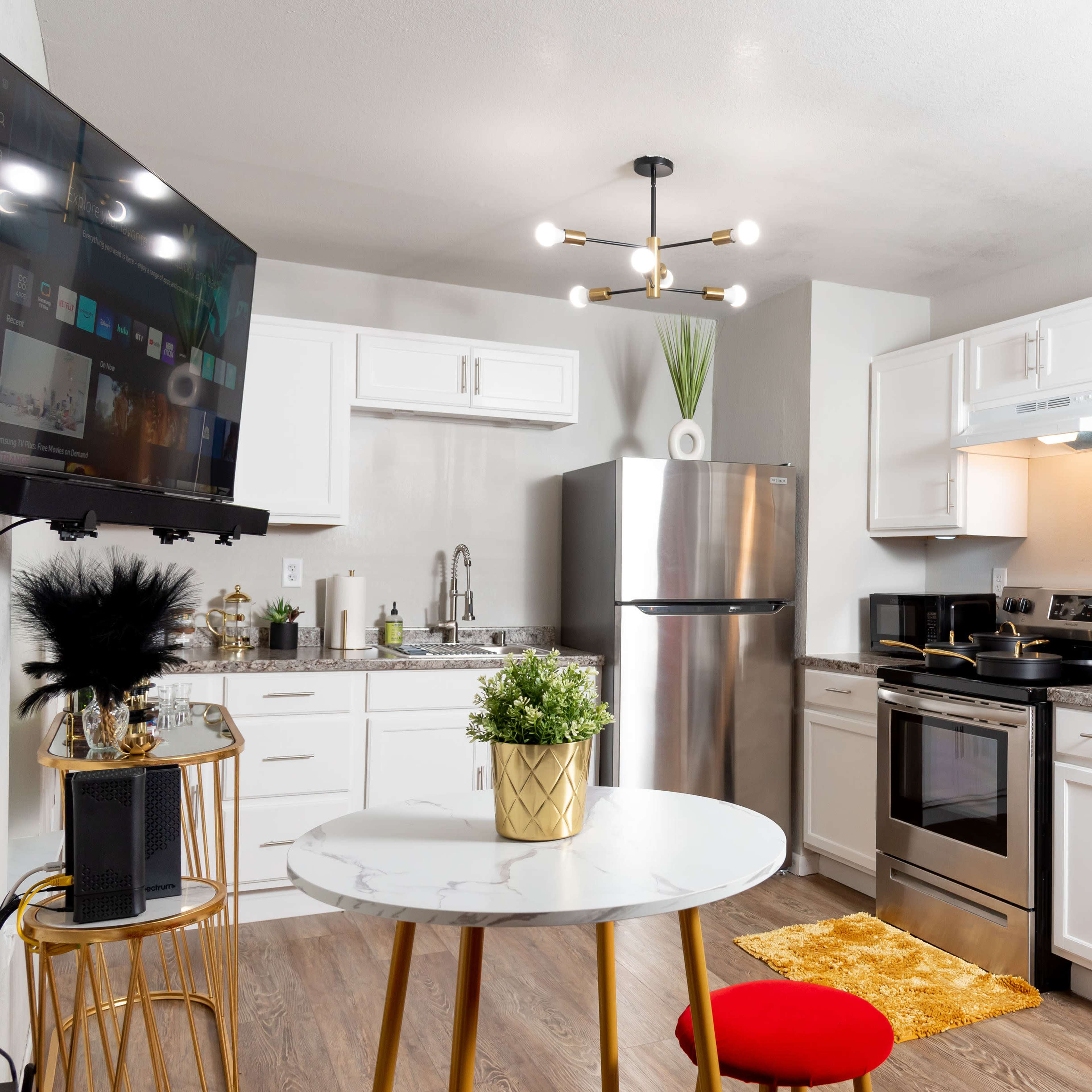 A modern kitchen with white cabinets, stainless steel appliances, and a small round dining table with a red chair.