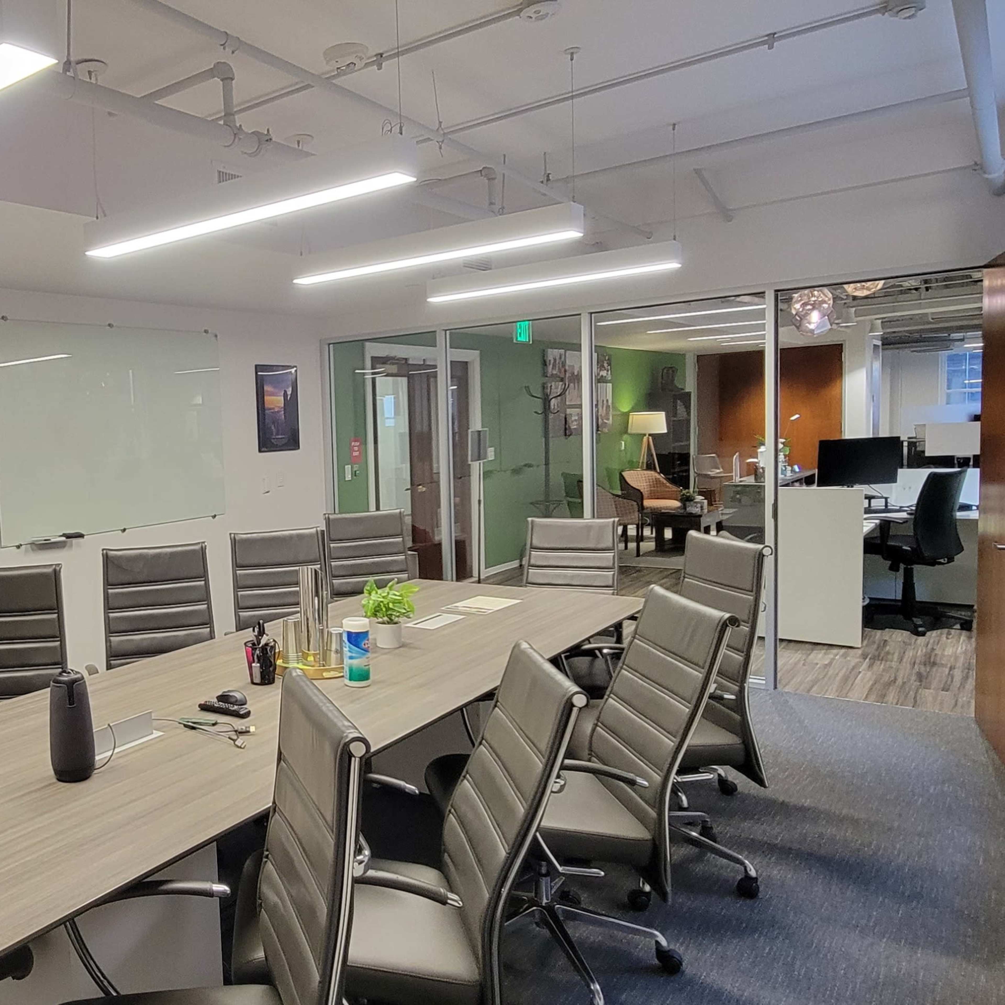 A conference room features a long wooden table surrounded by ergonomic chairs, with a whiteboard and glass wall in the background.