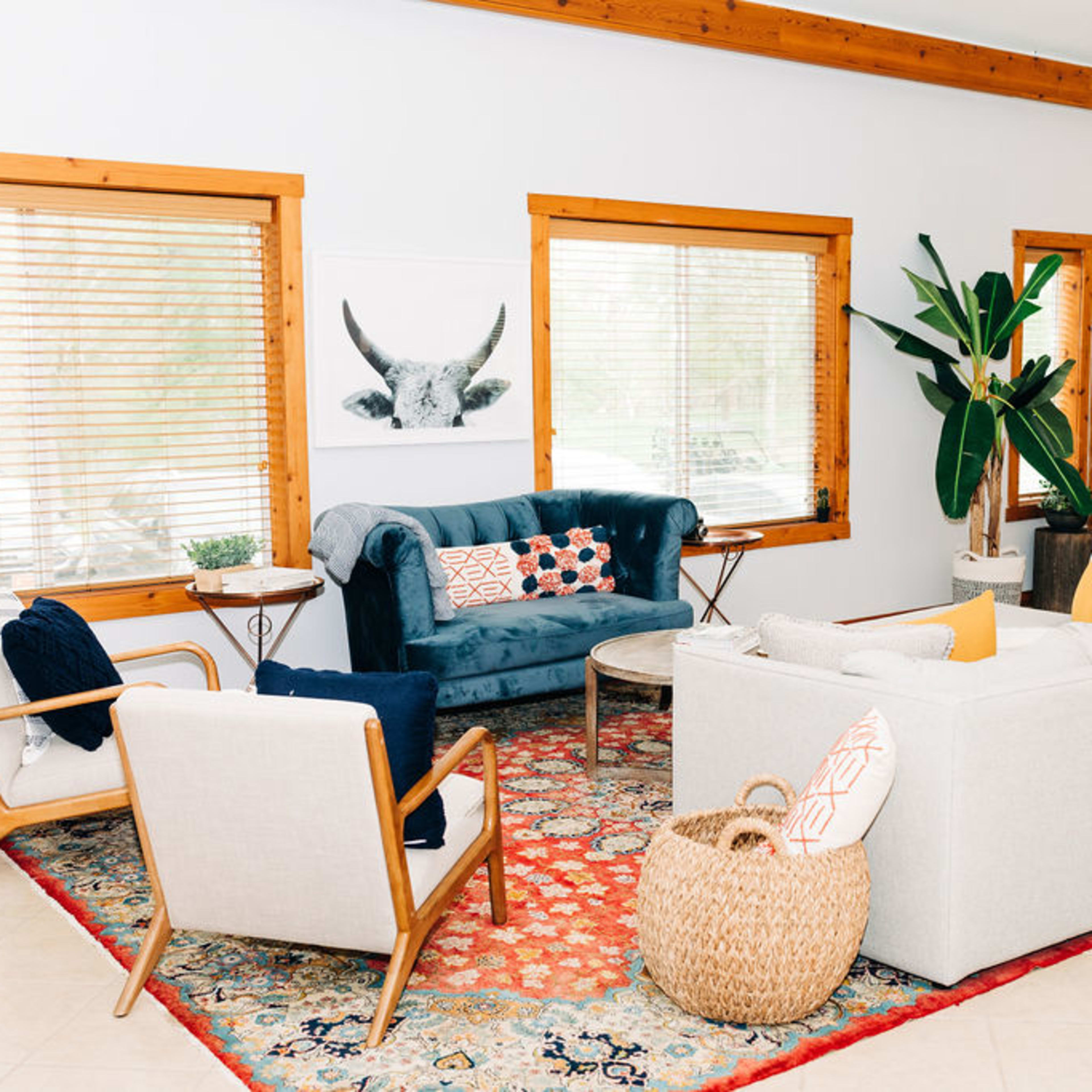 The living room features a sectional sofa, two armchairs, a round coffee table, and a large area rug, with large windows providing natural light.