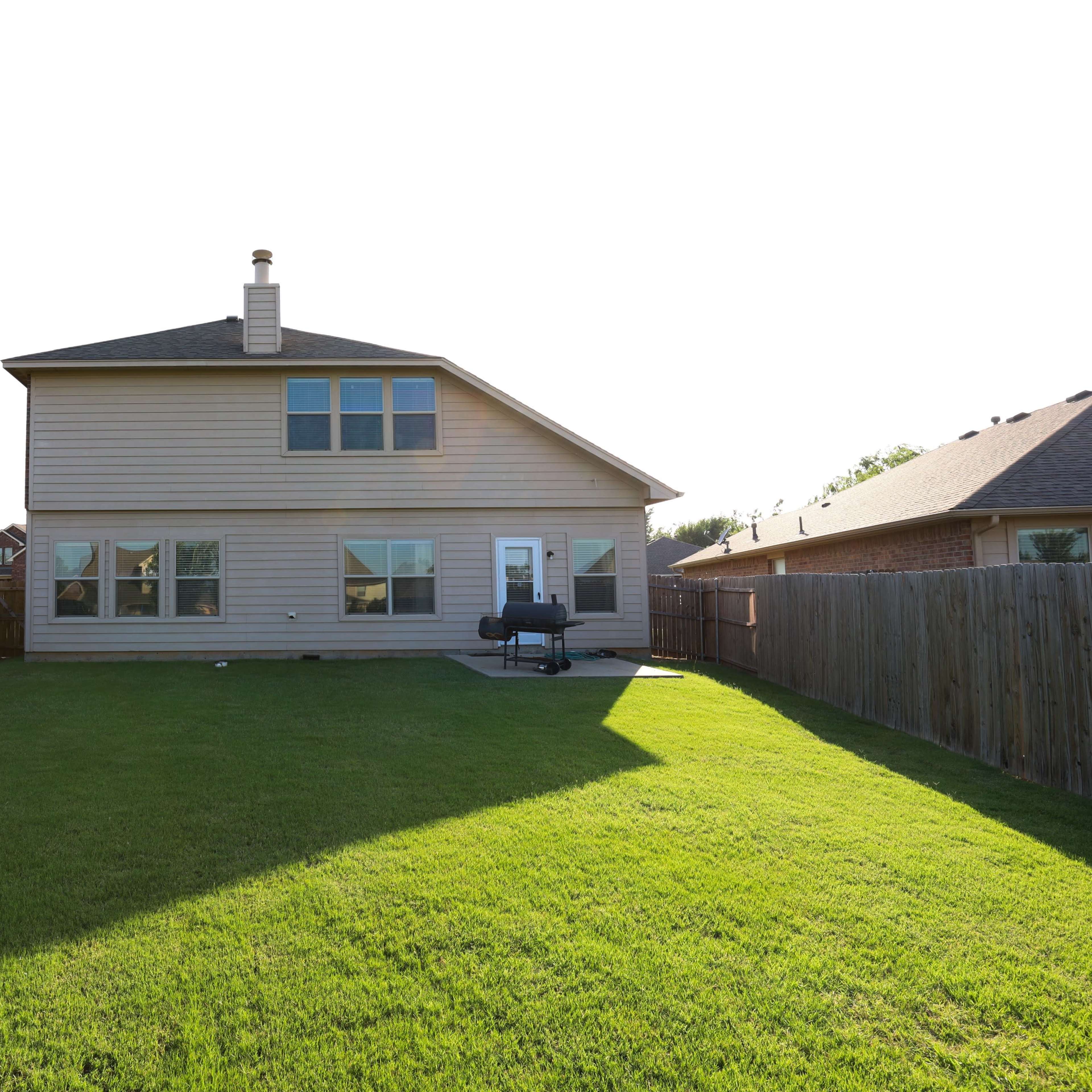 A backyard with a well-maintained lawn and a two-story house with large windows.