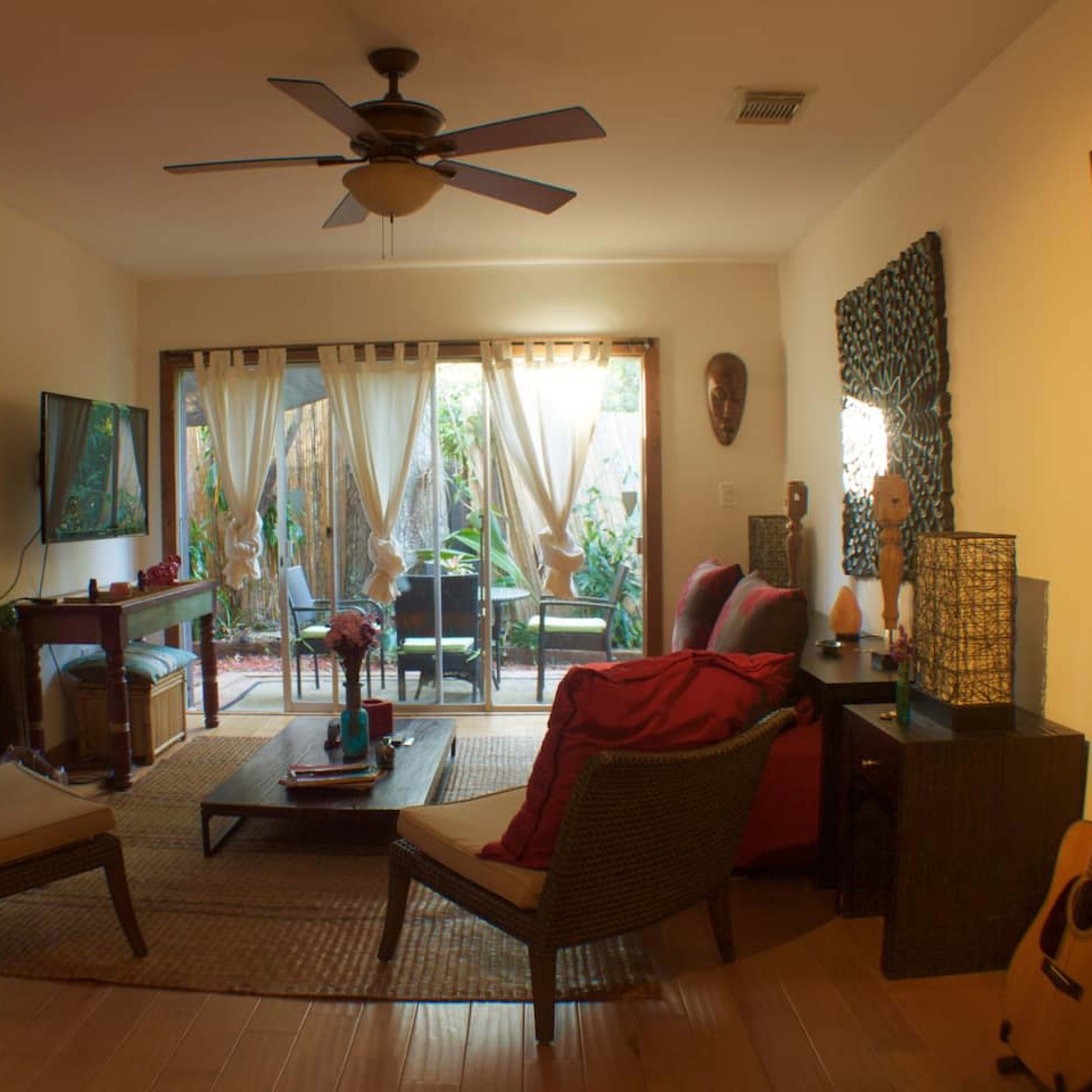 A cozy living room featuring a seating area with two chairs, a coffee table, and a view of a small garden through sheer curtains.