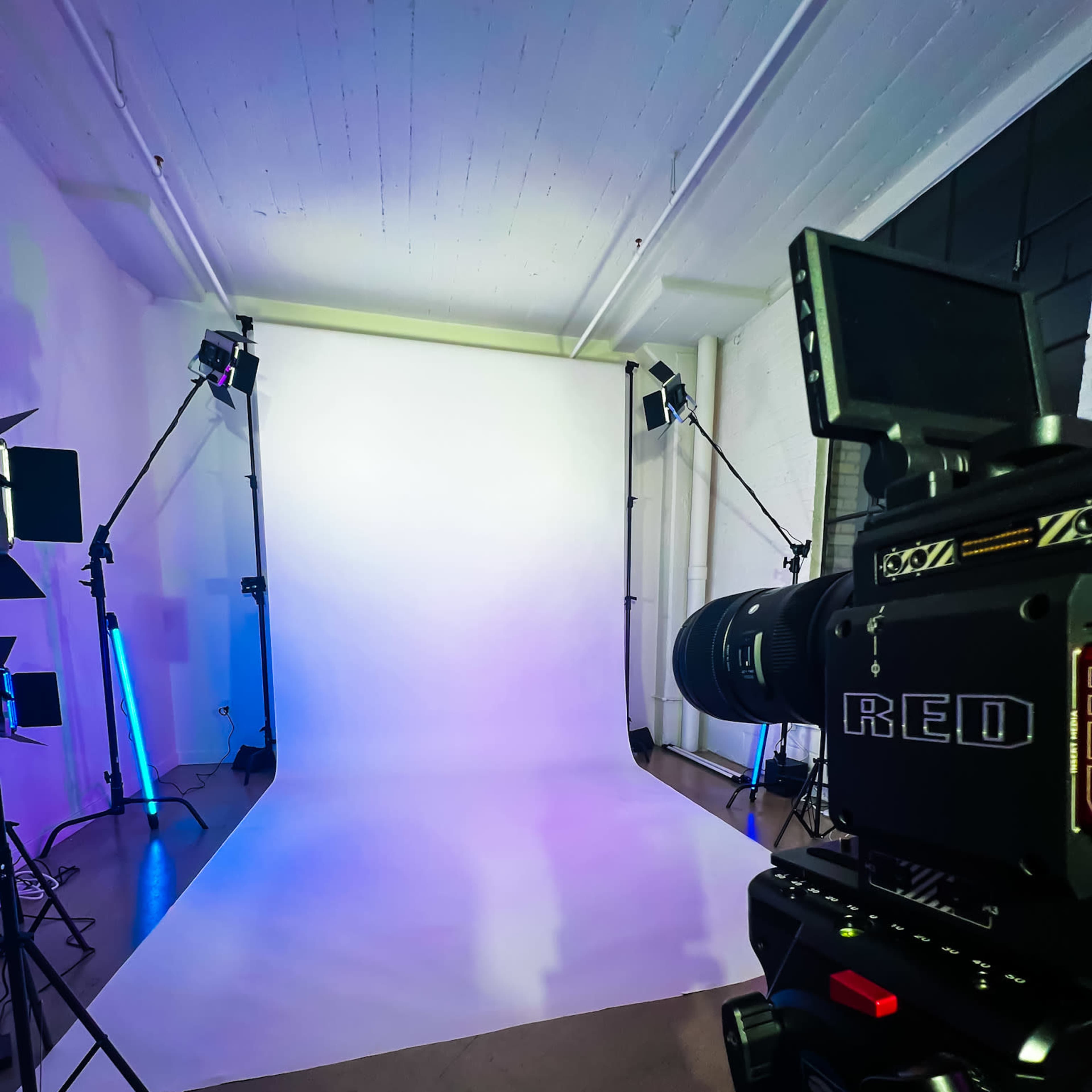 A professional photography studio features a white backdrop with lighting equipment and a RED camera positioned in the foreground.