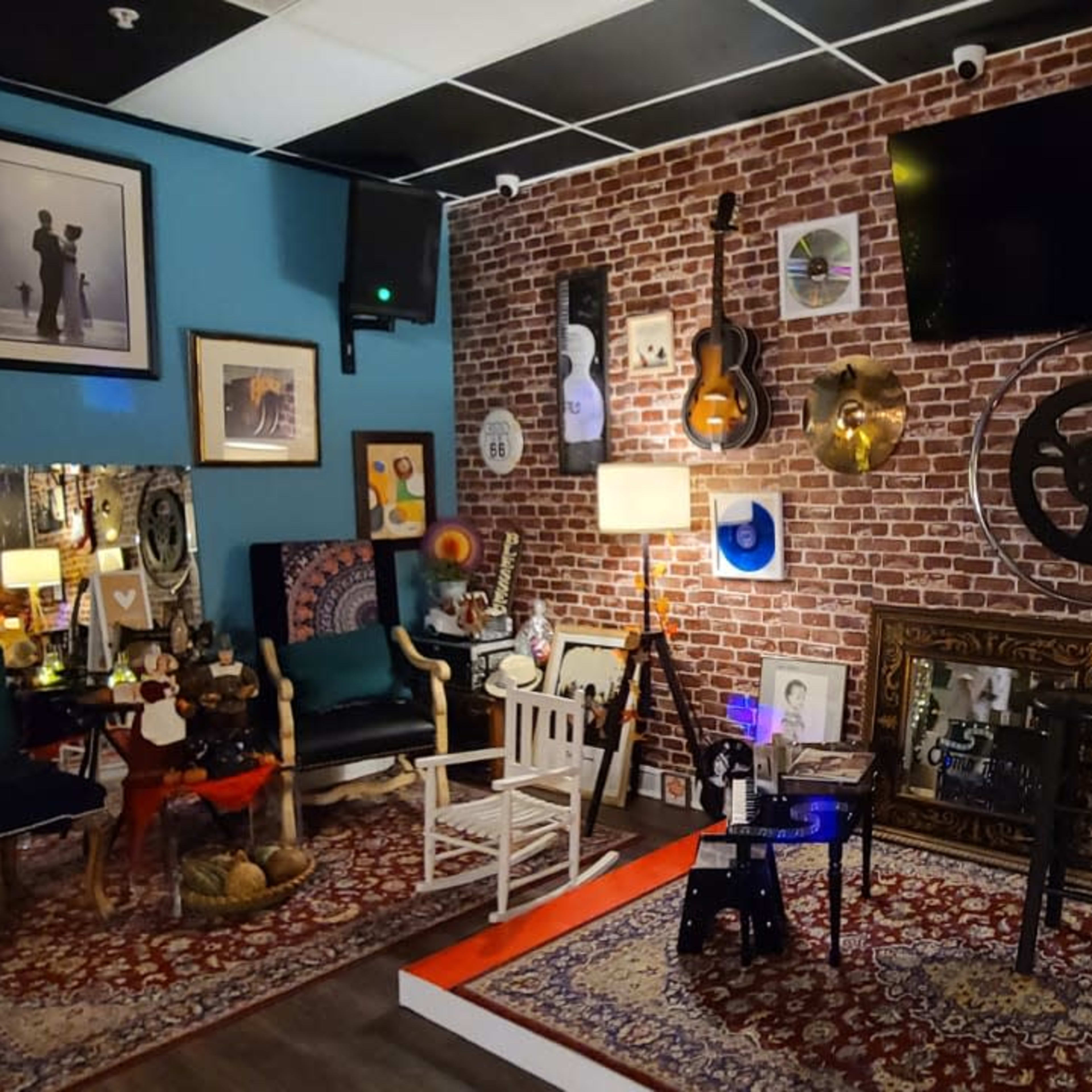 A cozy room with a brick wall adorned with musical instruments, framed pictures, and decorative items, including a guitar and vinyl records.