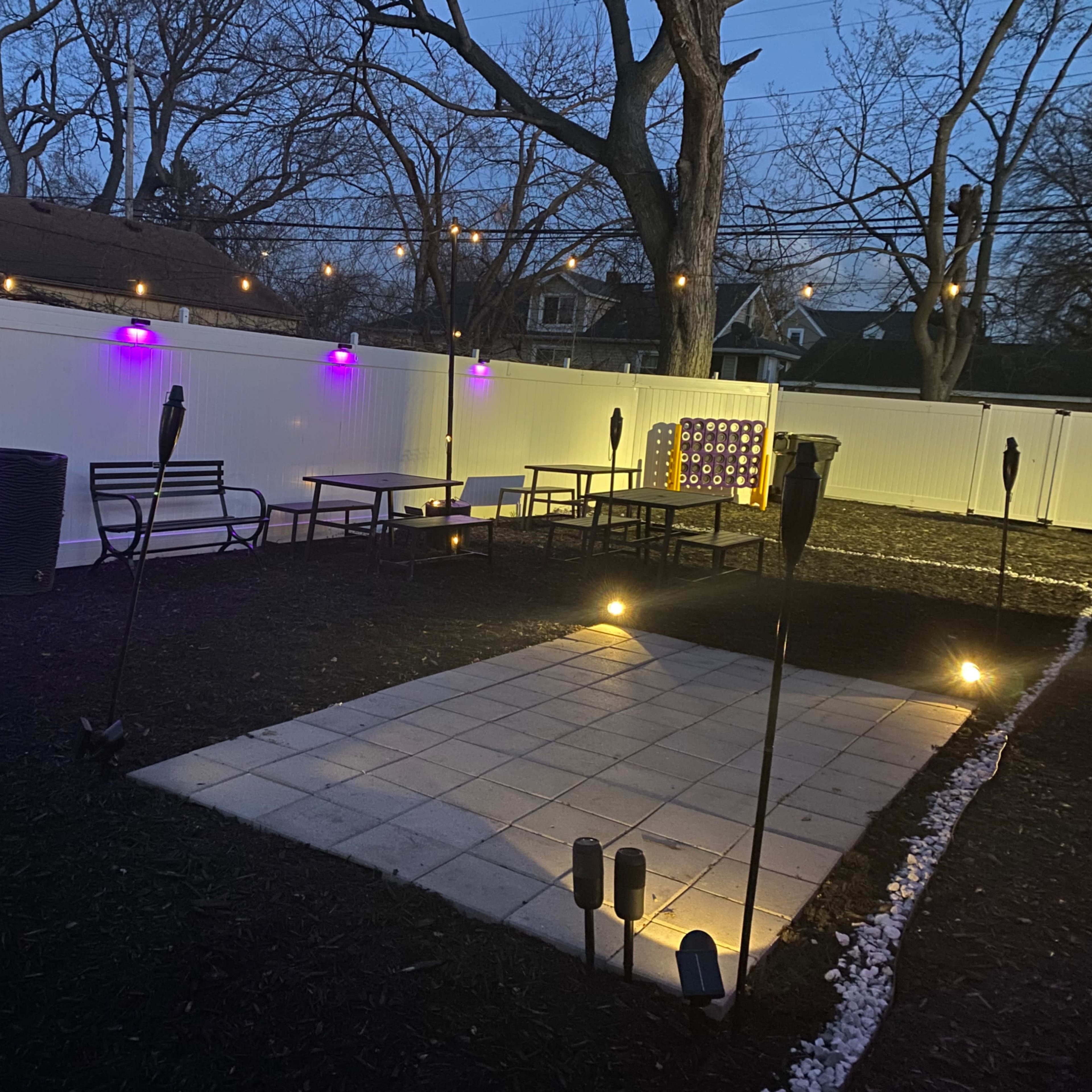 An outdoor patio area with purple lights, seating arrangements, and a paved square surrounded by tiki torches.
