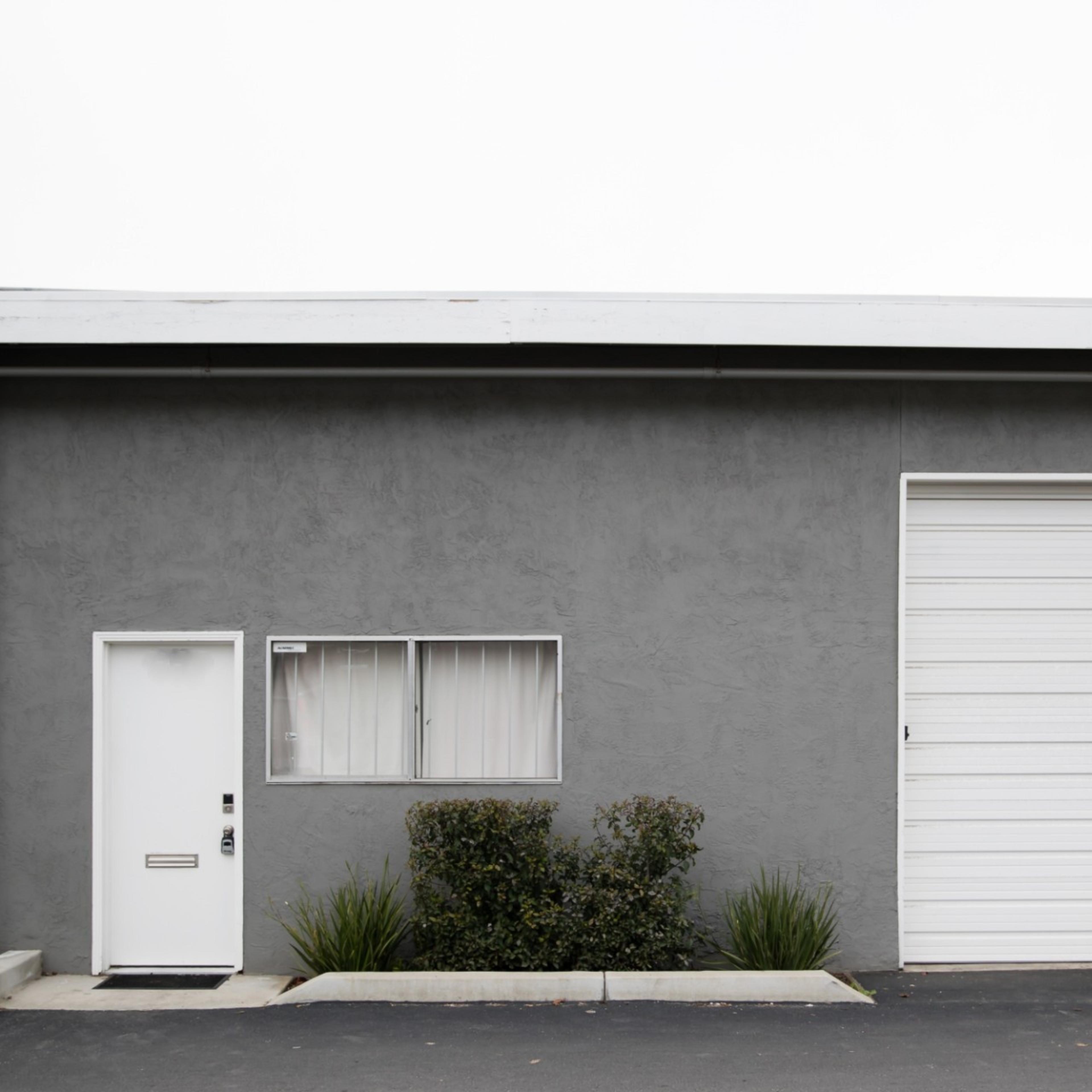 A gray building facade with a small door, a window, and a large white garage door.