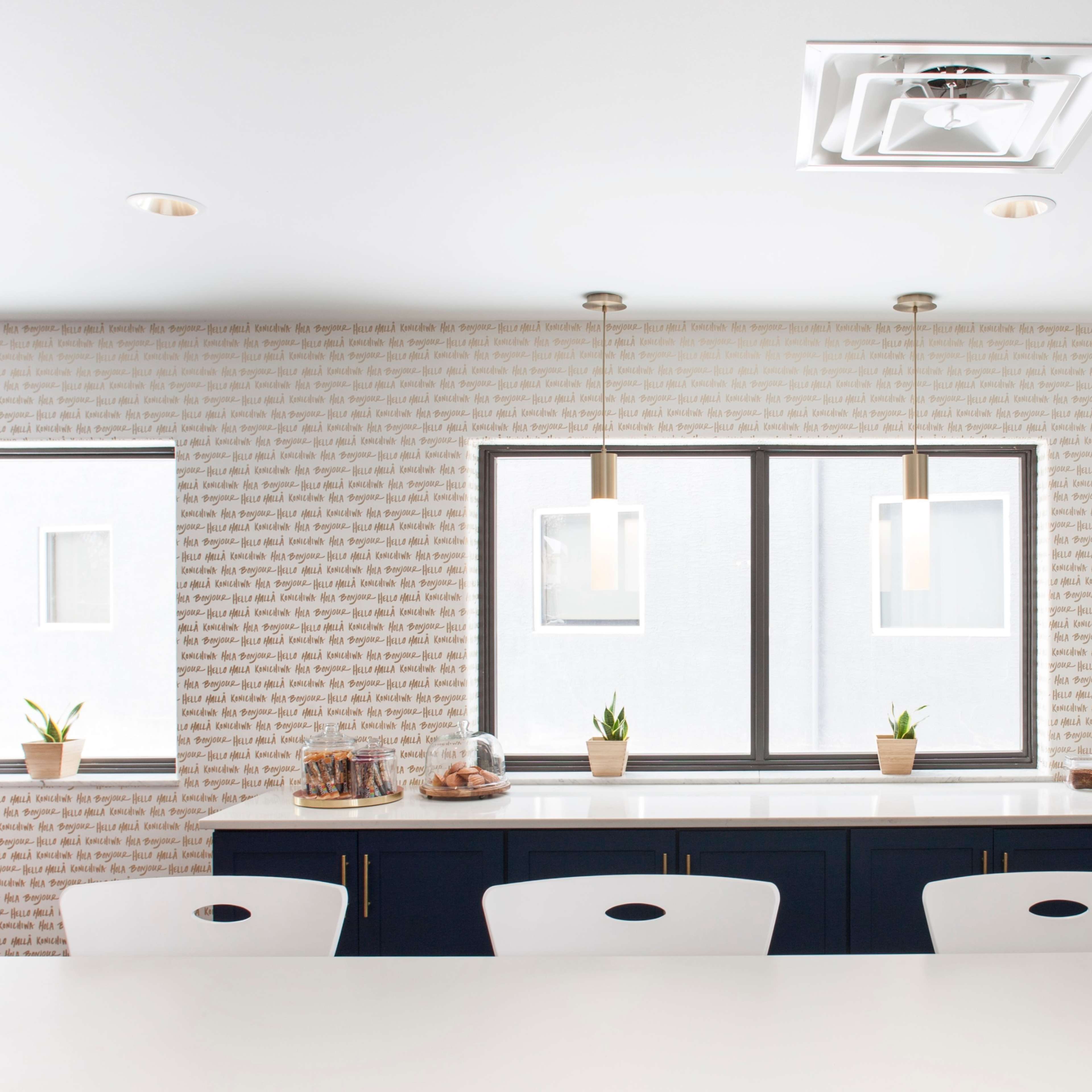 A modern kitchen features a white table and dark cabinets against a wall adorned with text wallpaper and large windows.