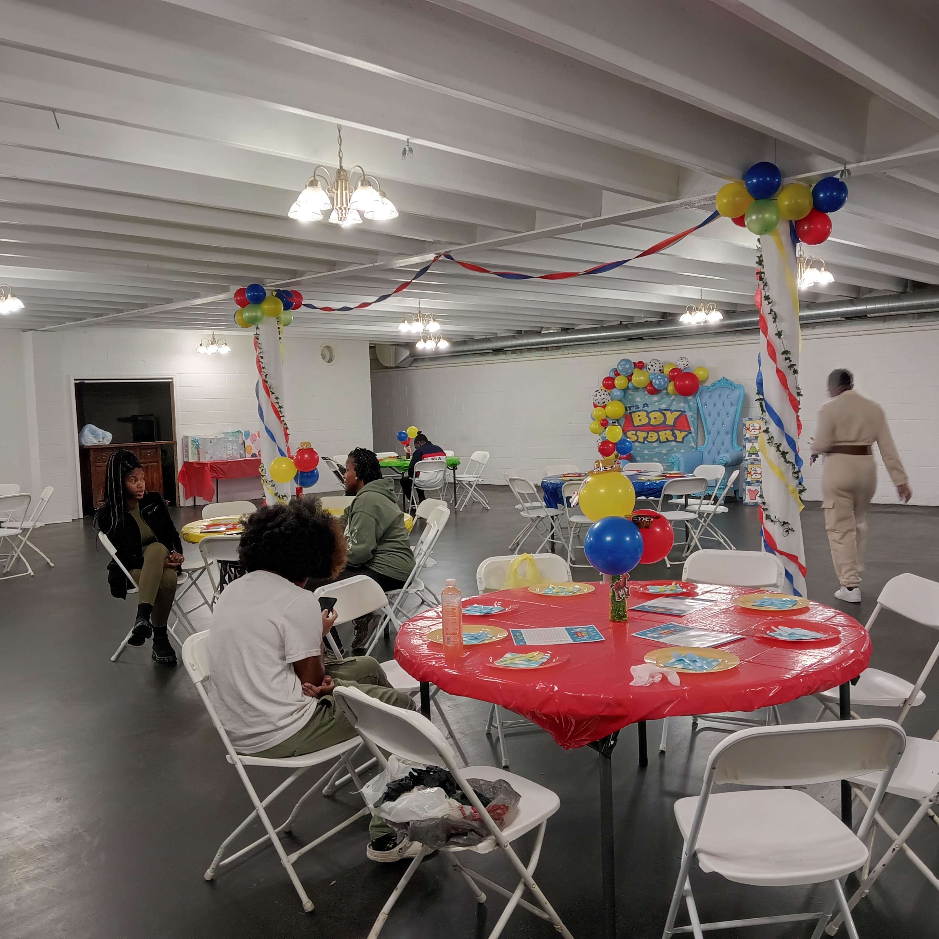 A decorated room with tables covered in red tablecloths, balloons, and a birthday banner, set up for a celebration.