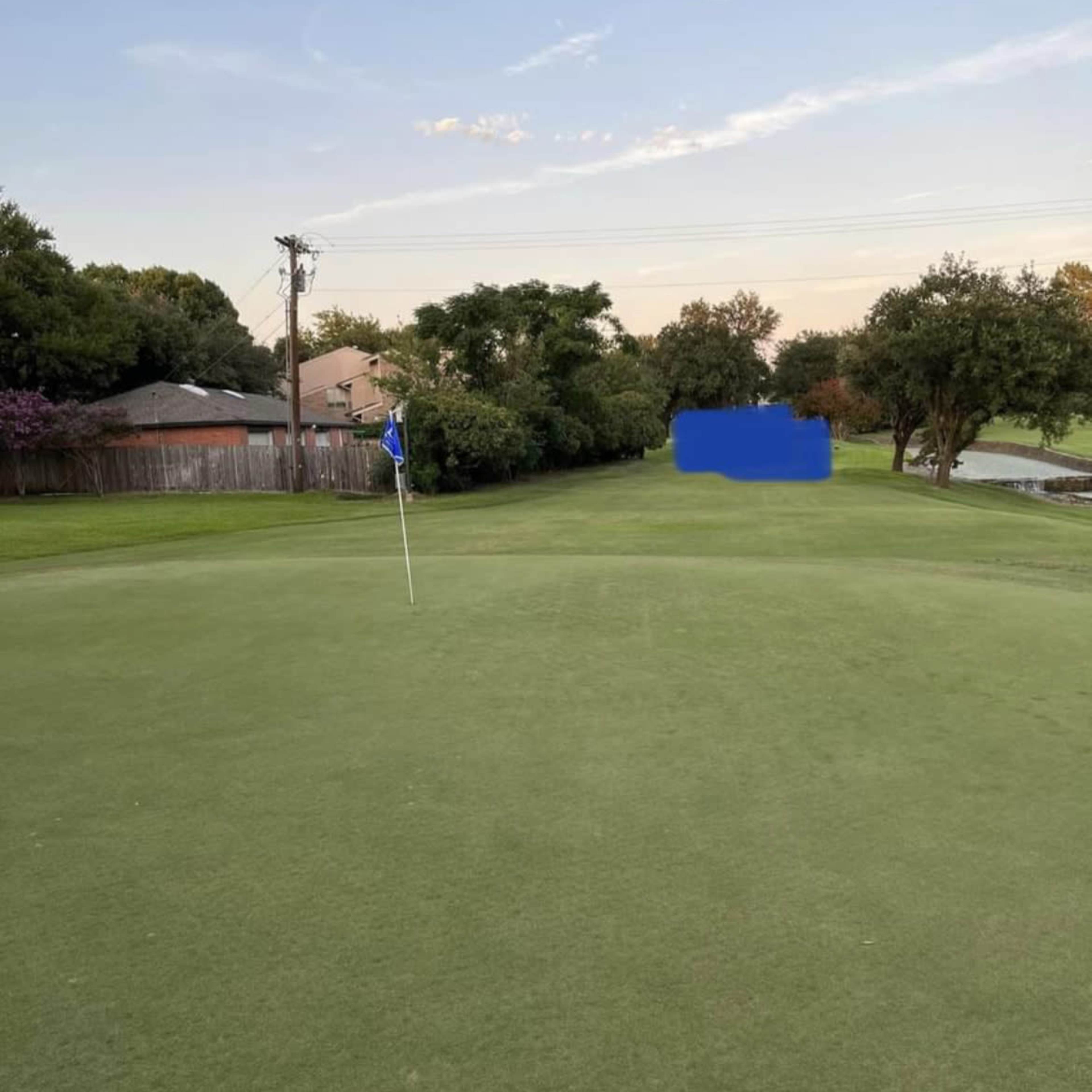 A golf course putting green with a flagstick in the hole and a golf ball positioned nearby.