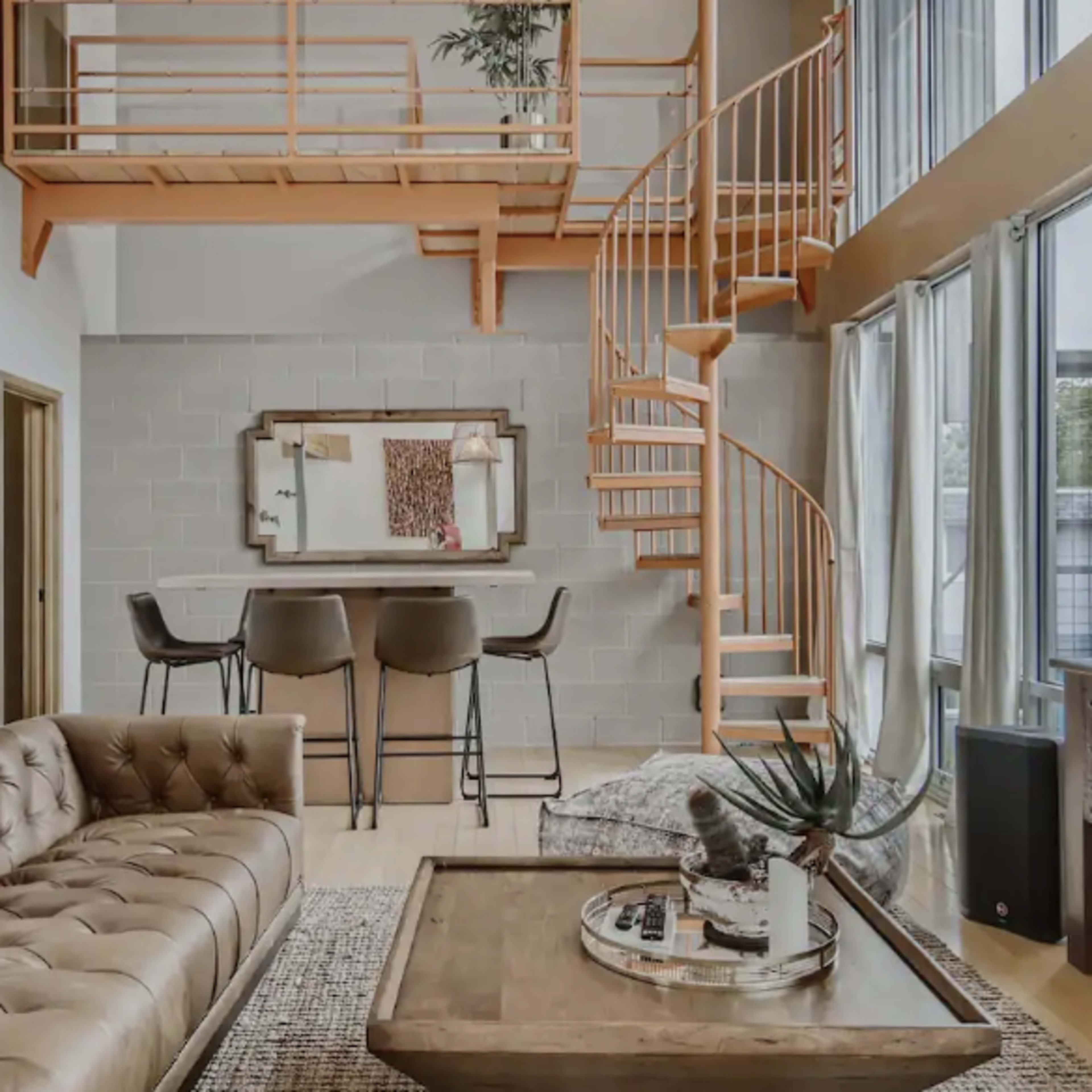 A modern living space featuring a spiral staircase, a leather sofa, and a dining table with bar stools.