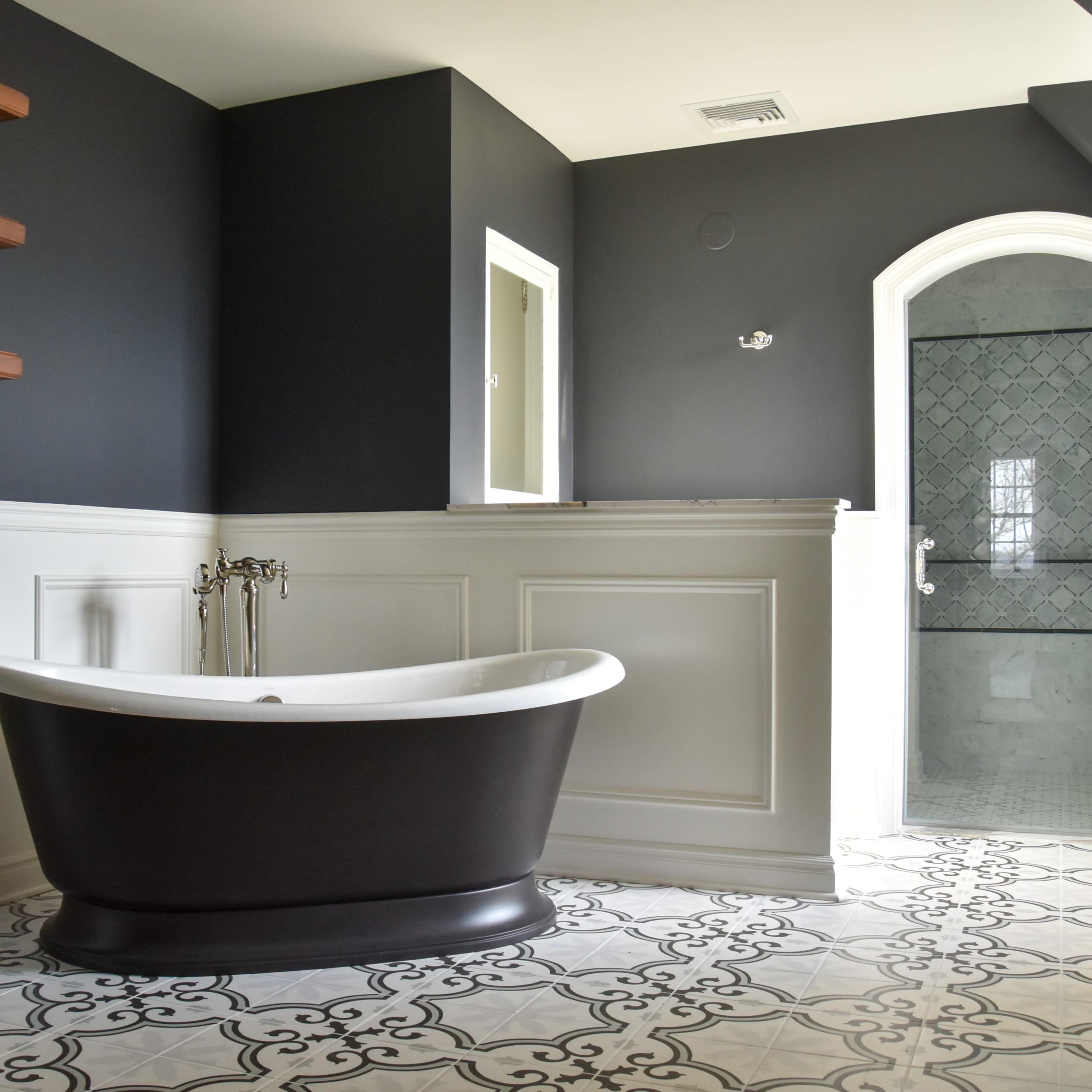 A bathroom featuring a black and white color scheme with a freestanding bathtub, patterned floor tiles, and a glass-enclosed shower.