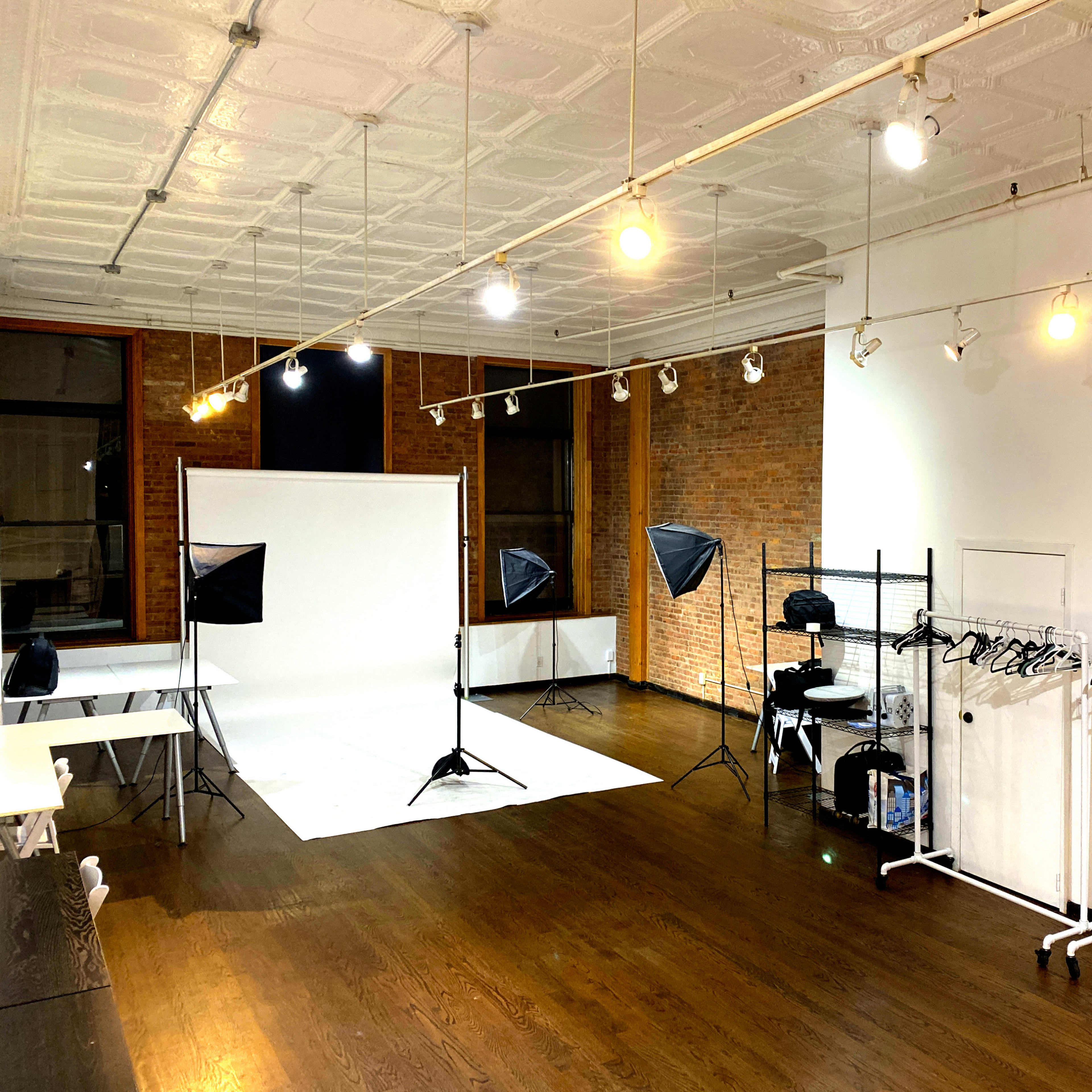 A photography studio with lighting equipment, a backdrop setup, and clothing racks arranged along the walls.