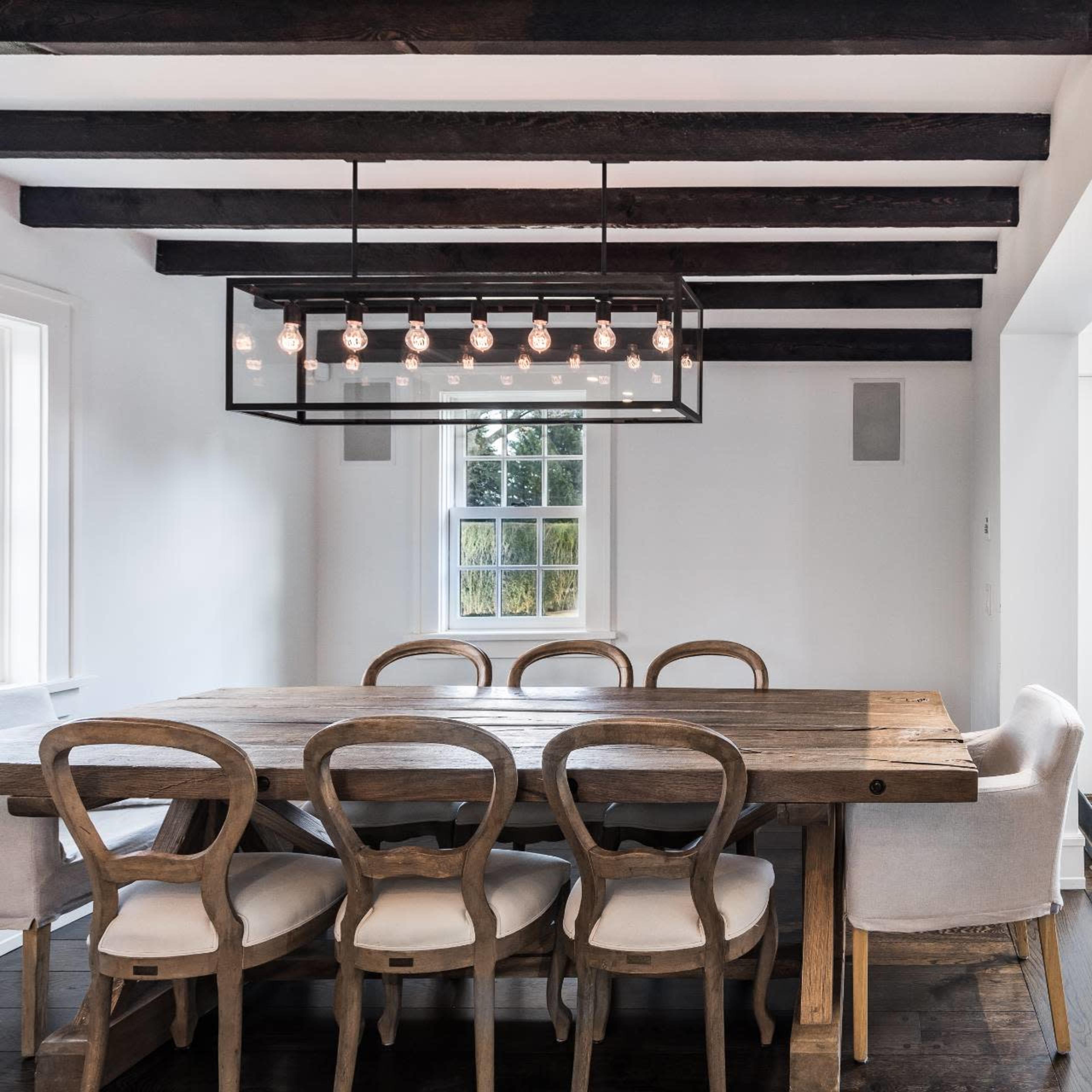 A modern dining area features a wooden table surrounded by six chairs, with a pendant light overhead and open doors leading to an outdoor patio.