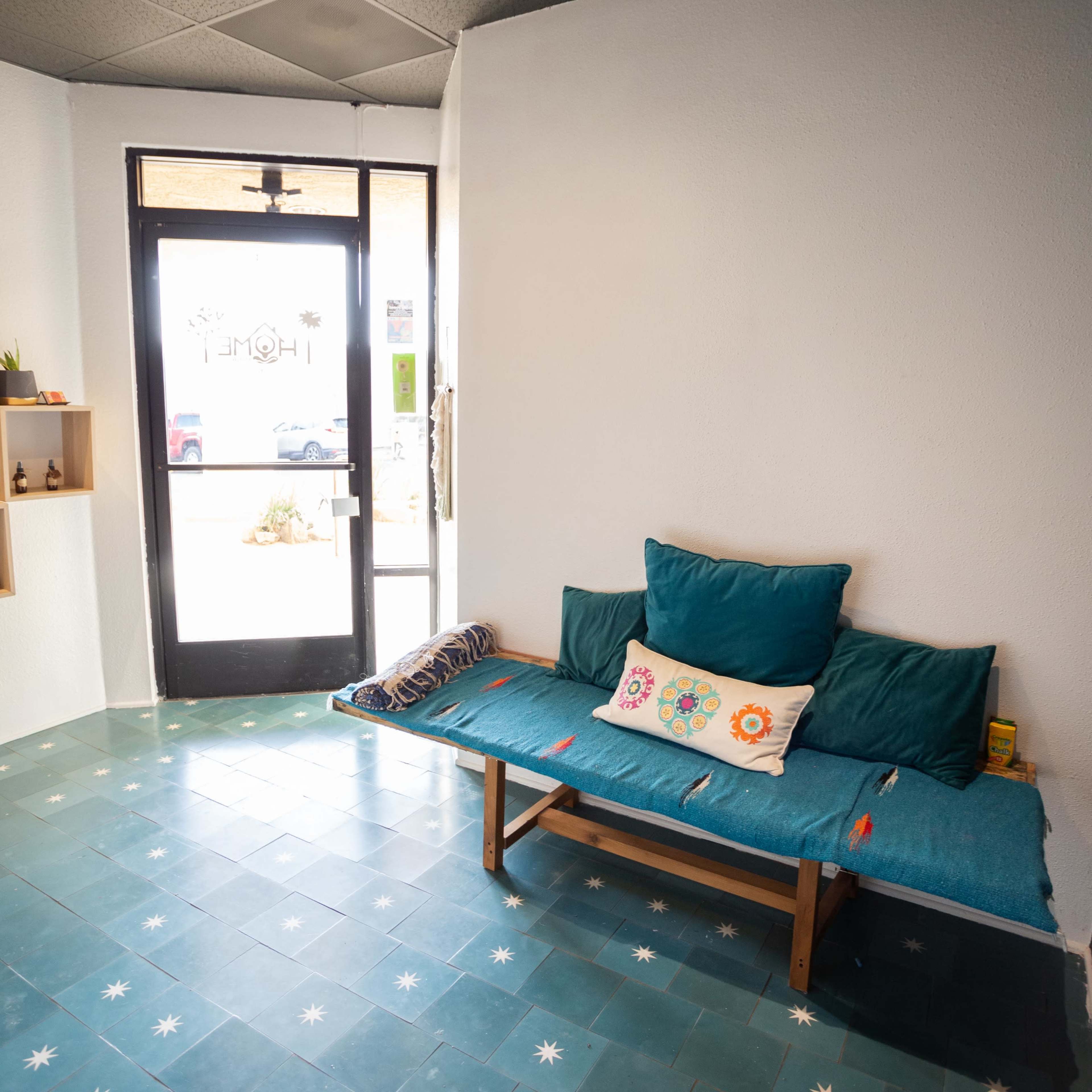 A small interior space featuring a wooden bench with teal cushions, a decorative pillow, and a door leading outside.