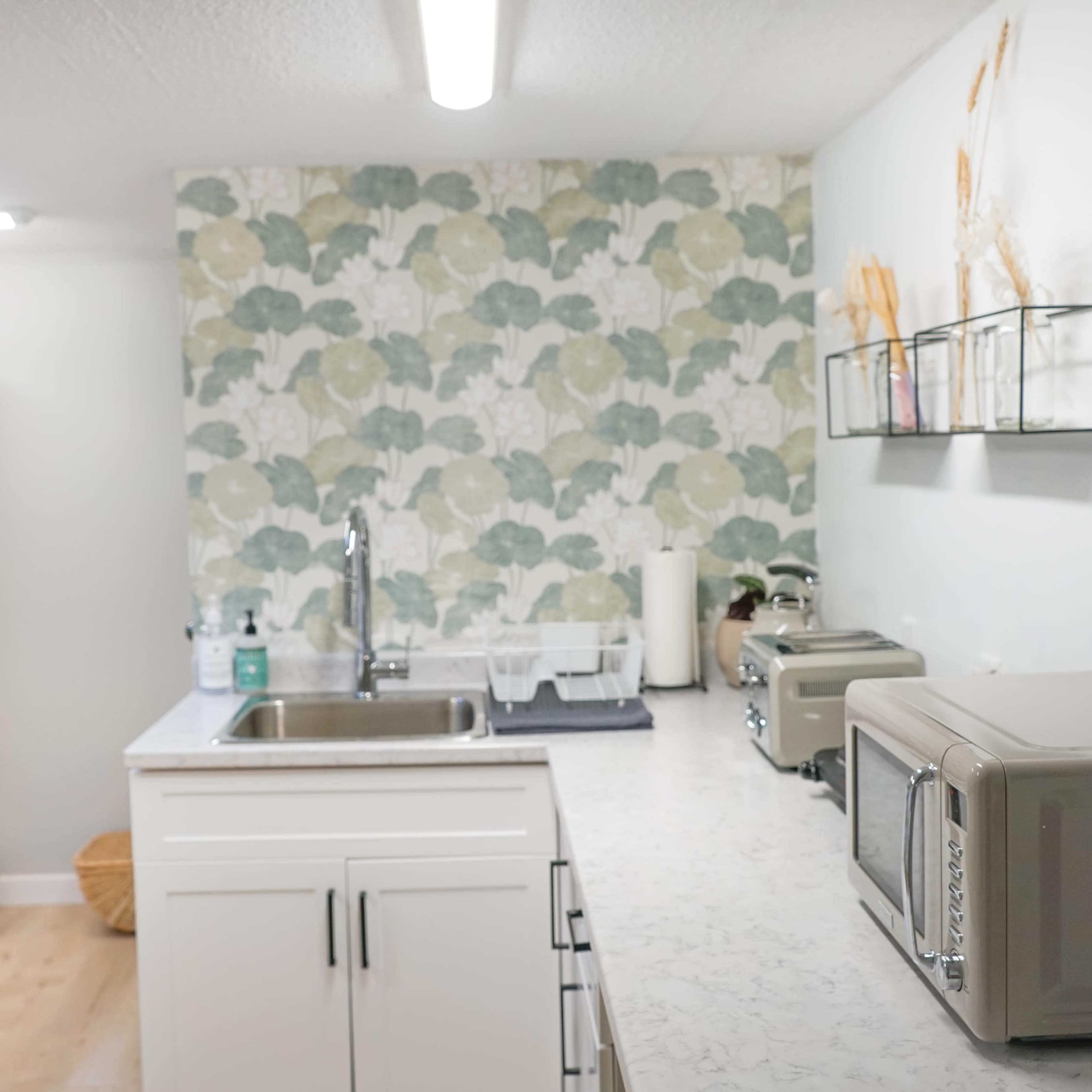 A modern kitchen with a marble countertop, a sink, an array of kitchen appliances, and a patterned floral wallpaper.