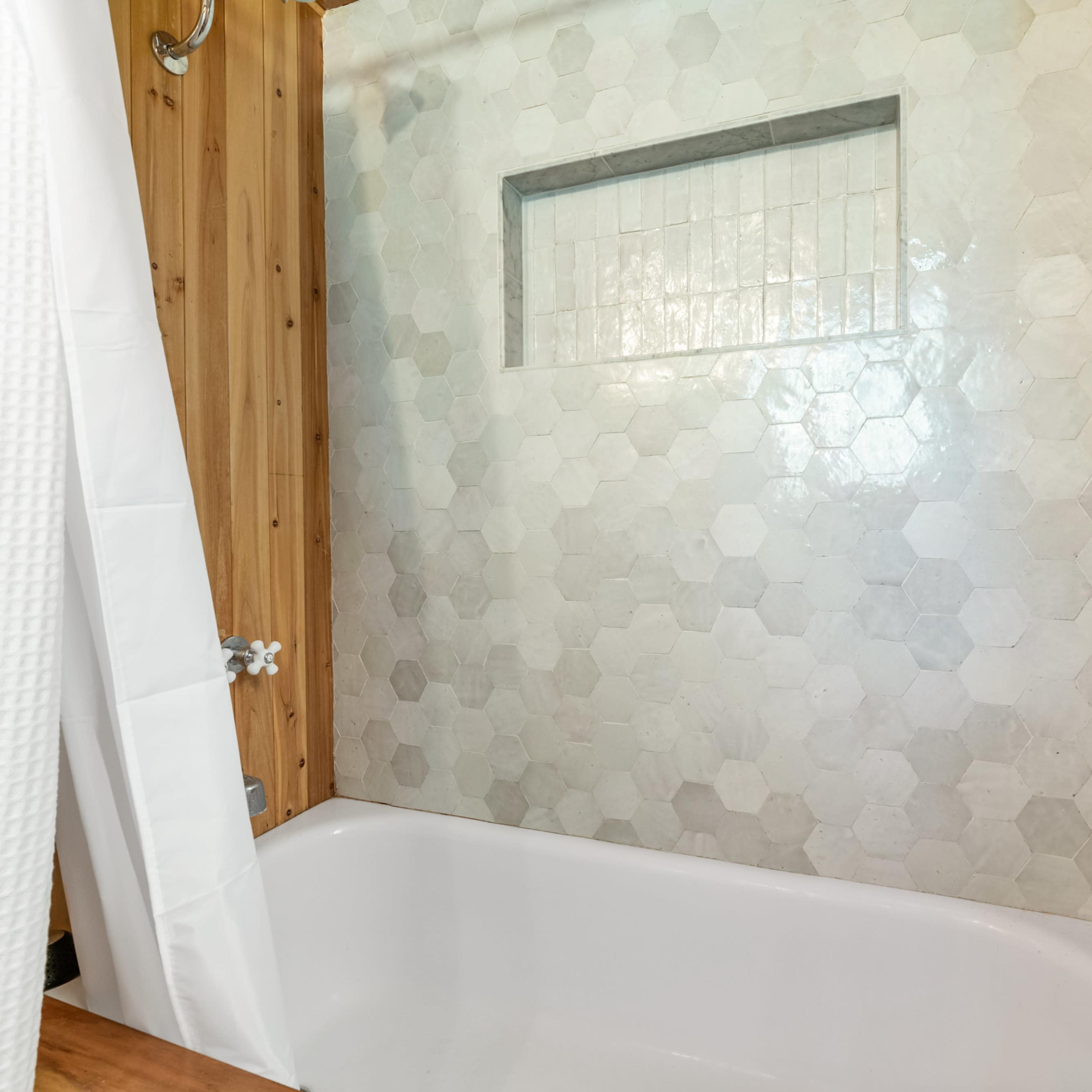 A bathtub with a hexagonal tile wall and wooden accents in a bathroom setting.