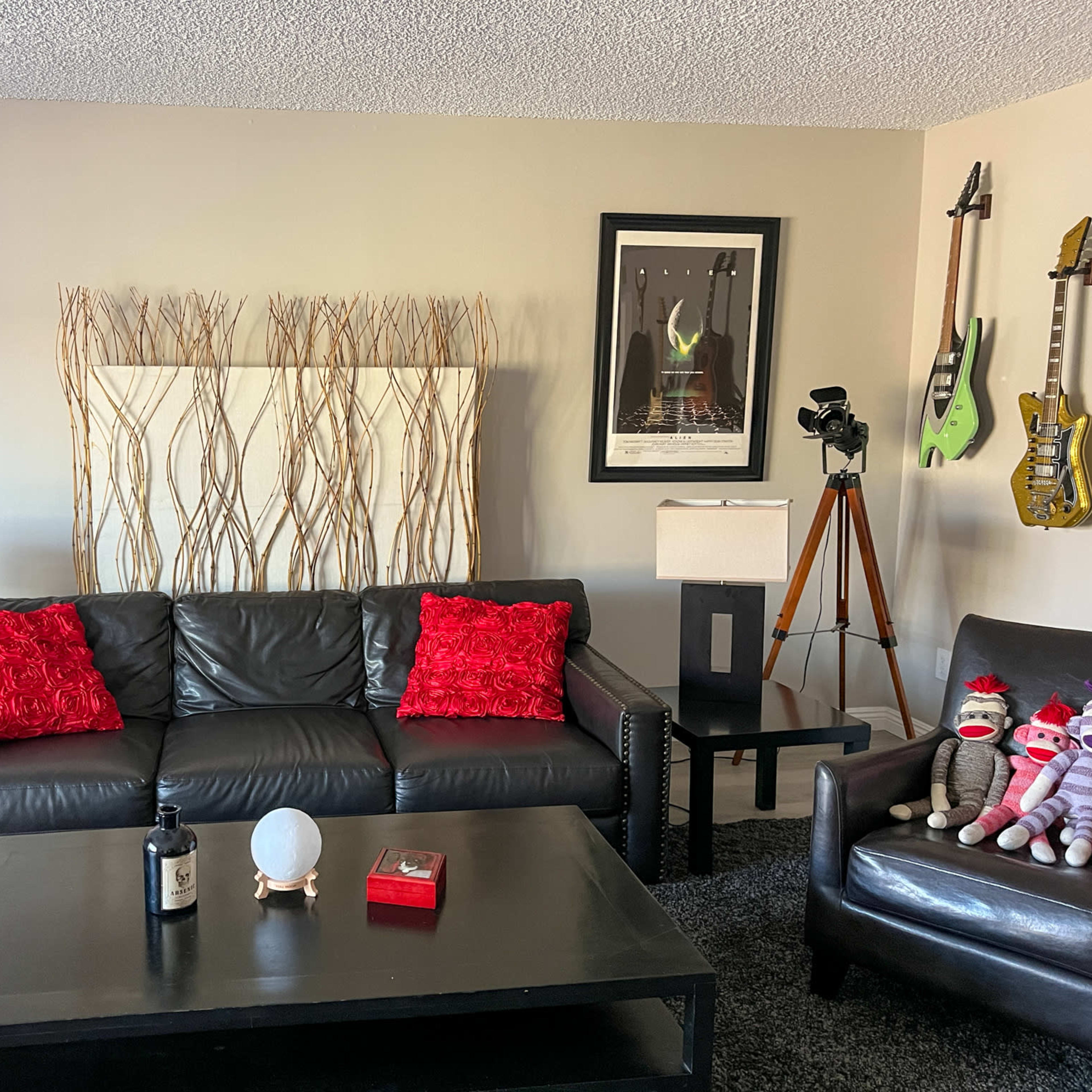 The living room features a black leather sofa with red pillows, accompanied by a black coffee table, decorative wall art, and guitars mounted on the walls.