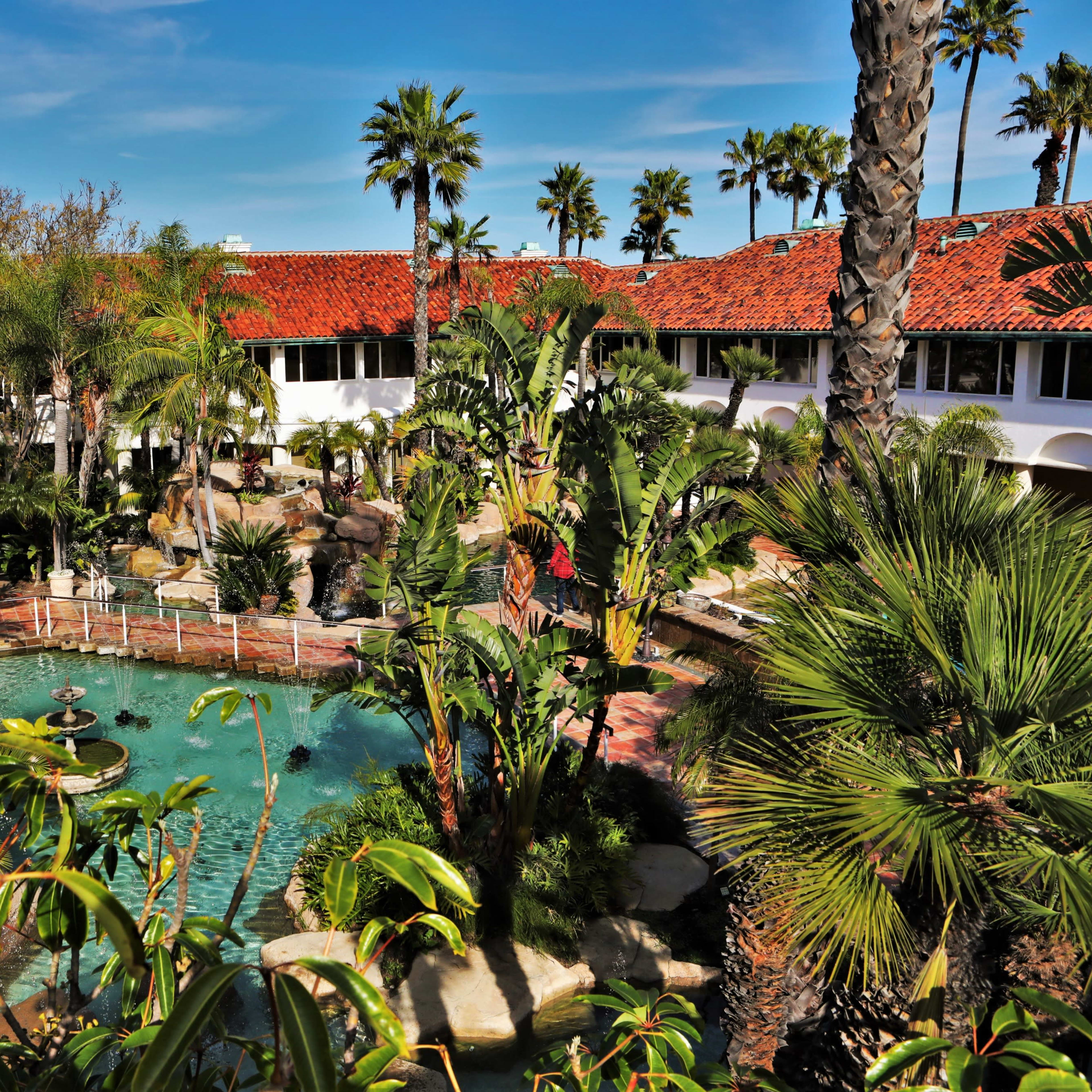 A tropical resort courtyard featuring a pool surrounded by palm trees and landscaped gardens.