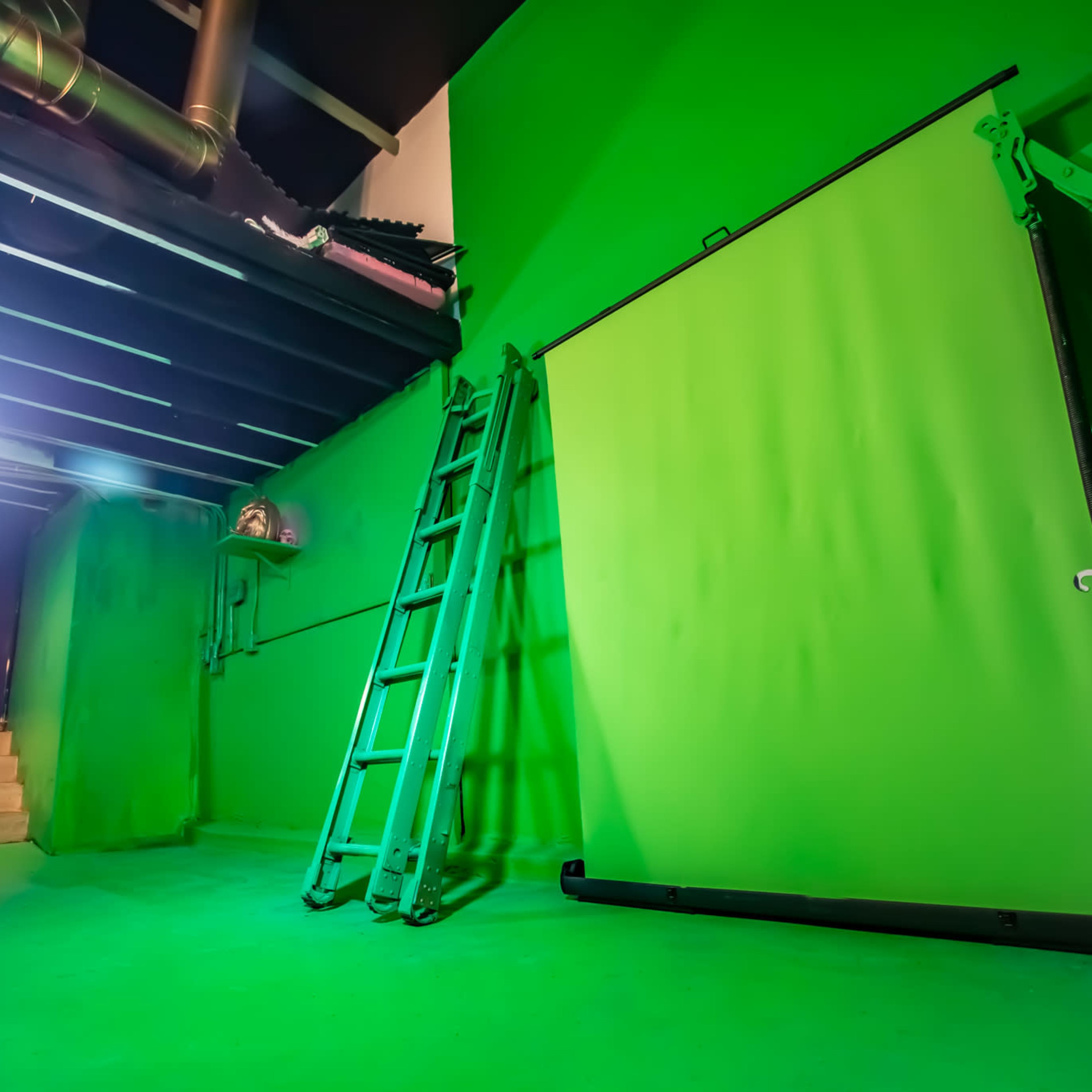 A green room with a ladder, a green backdrop, and a light source illuminating the space.