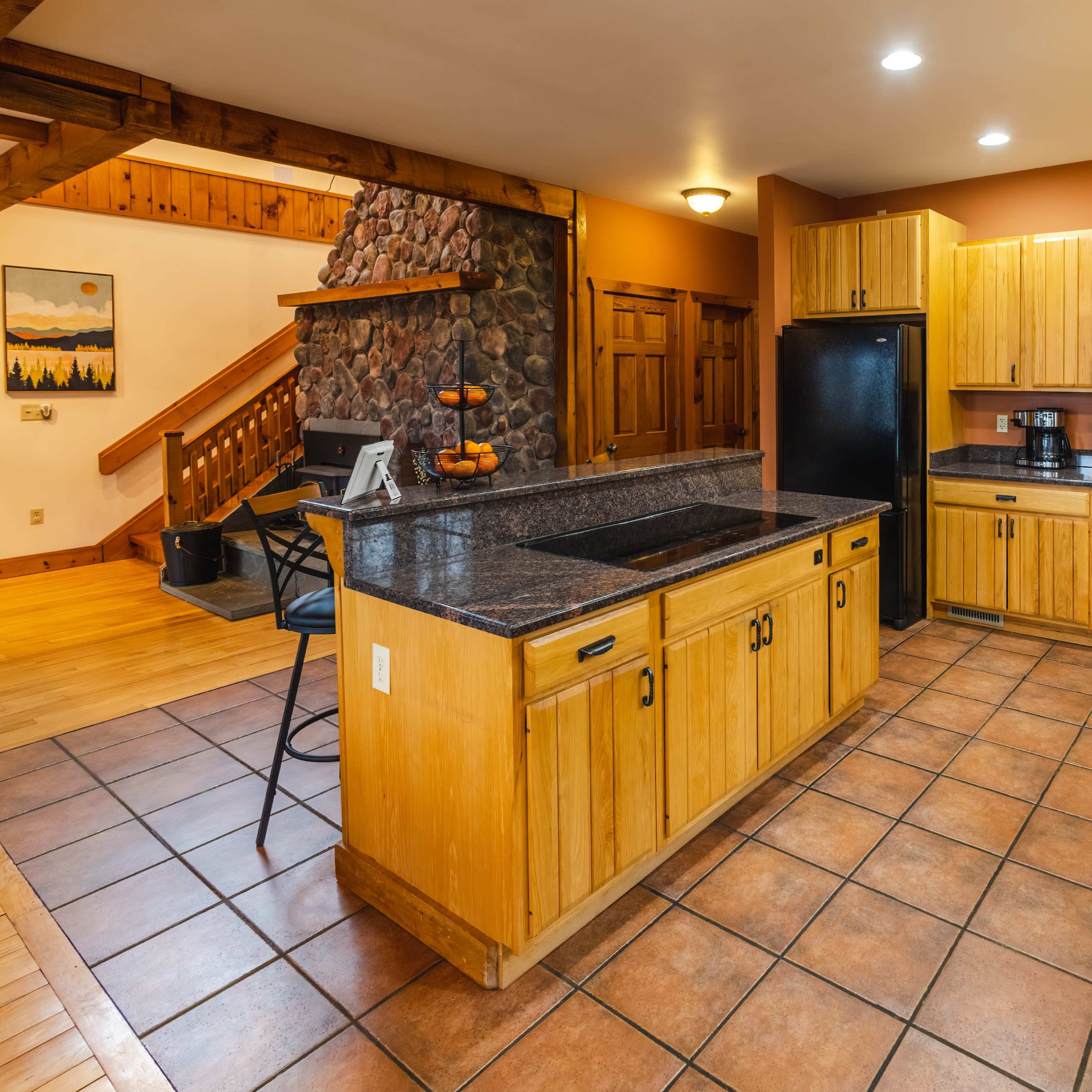 The kitchen features wooden cabinets, a dark granite countertop, and tile flooring, with appliances and utensils arranged along the walls.