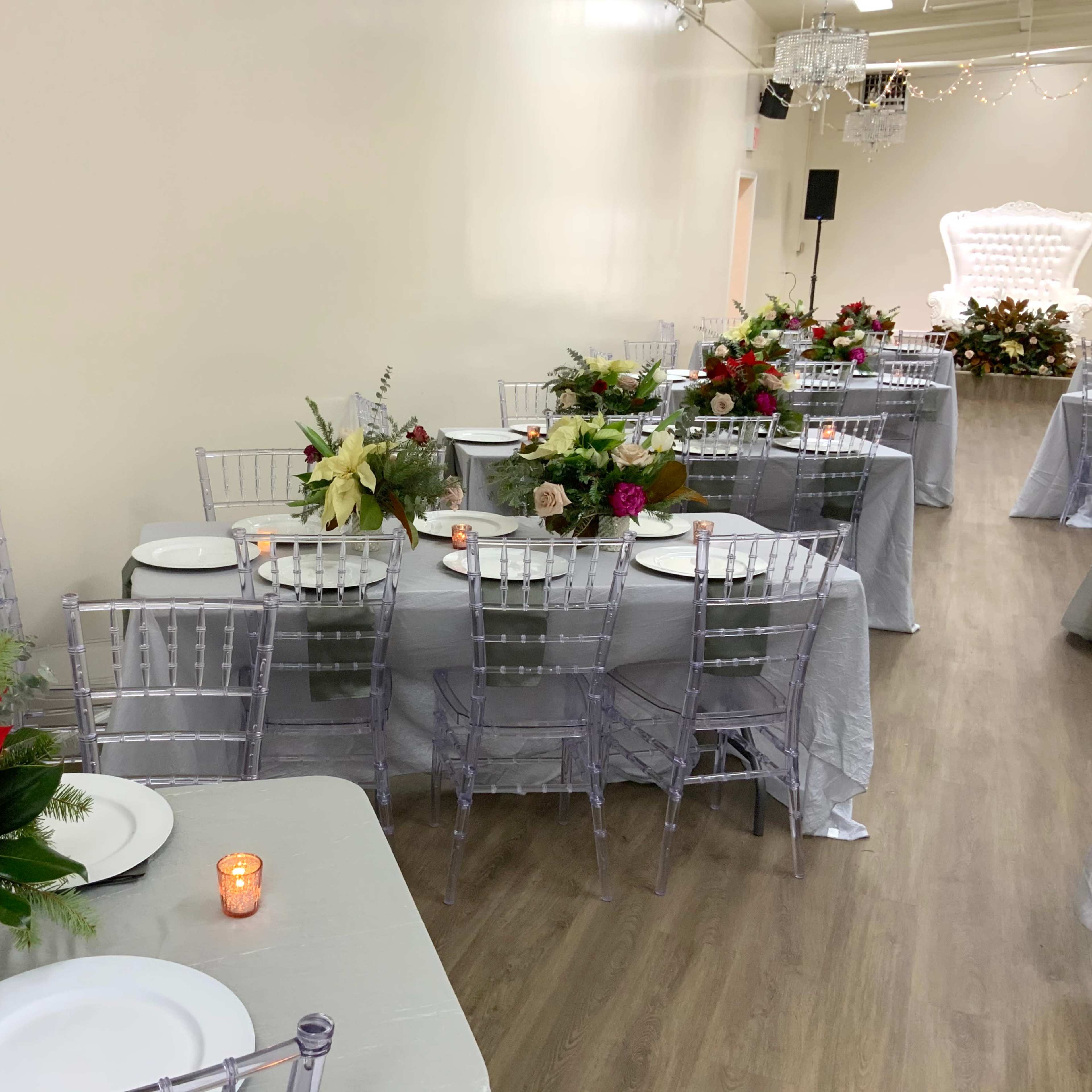 A decorated dining area with silver tablecloths, floral centerpieces, and place settings on tables arranged in a row.