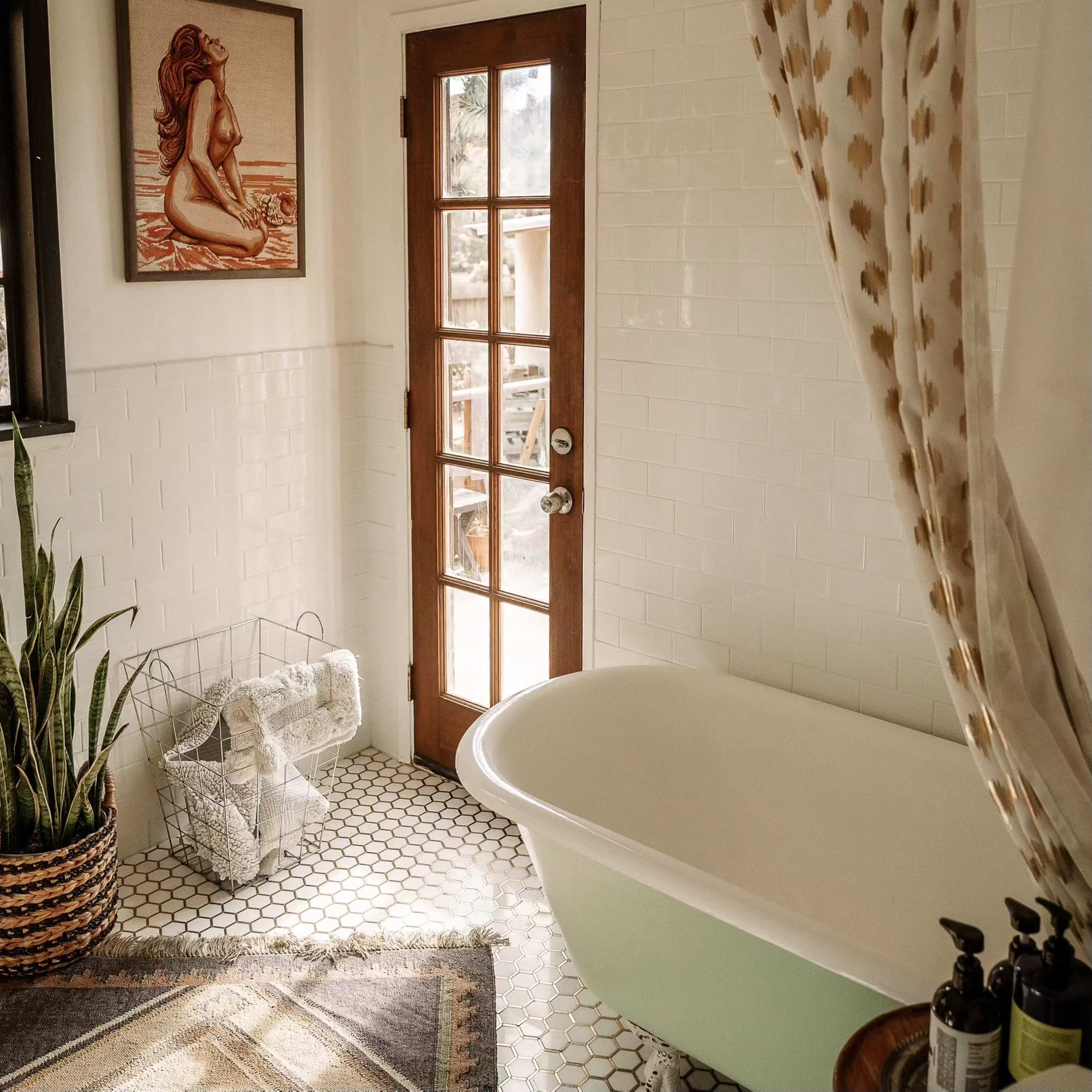 A bathroom features a freestanding tub, a door with multiple glass panes, and a potted plant beside a wire basket holding towels.