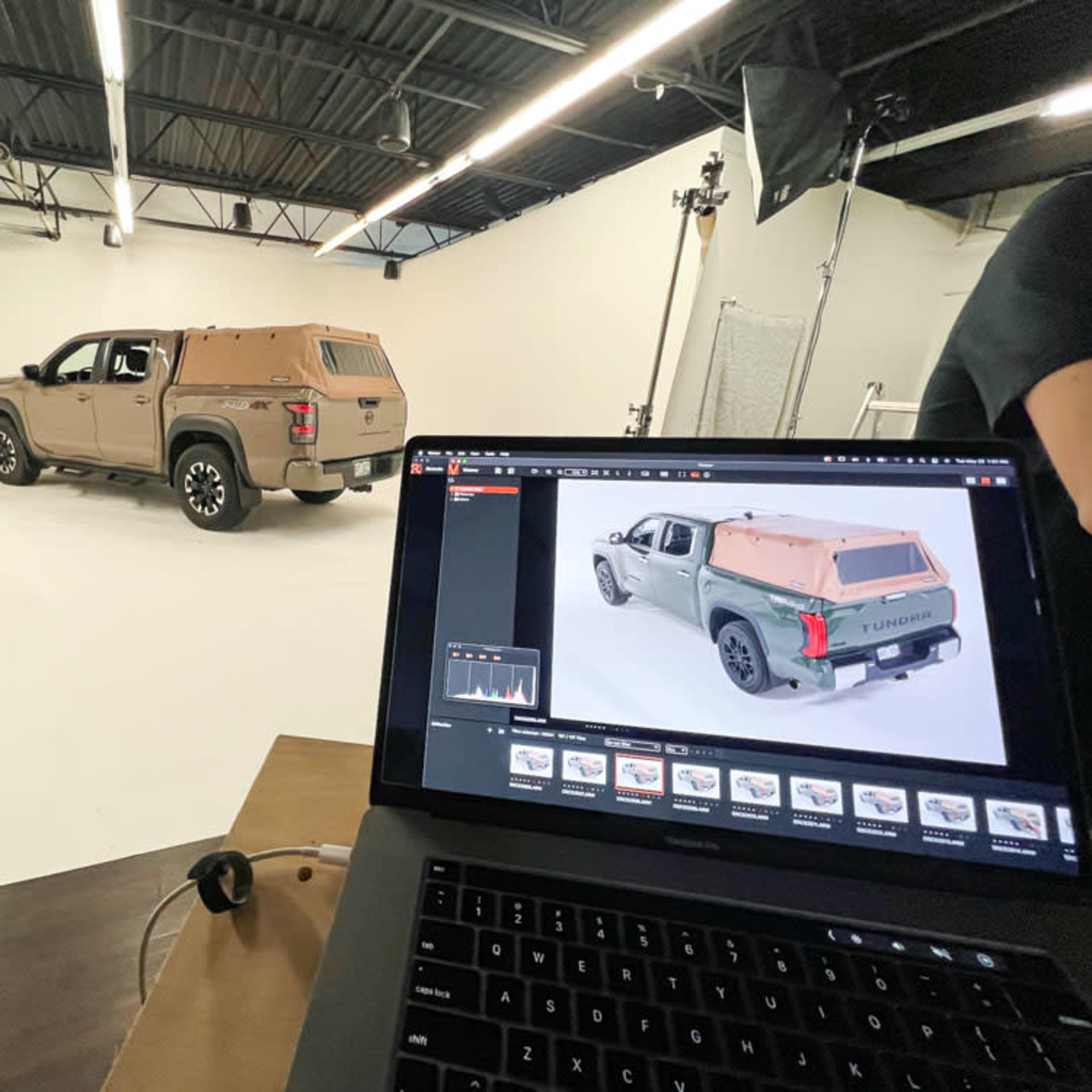 A vehicle is parked in a photography studio with a laptop displaying images of the same vehicle.