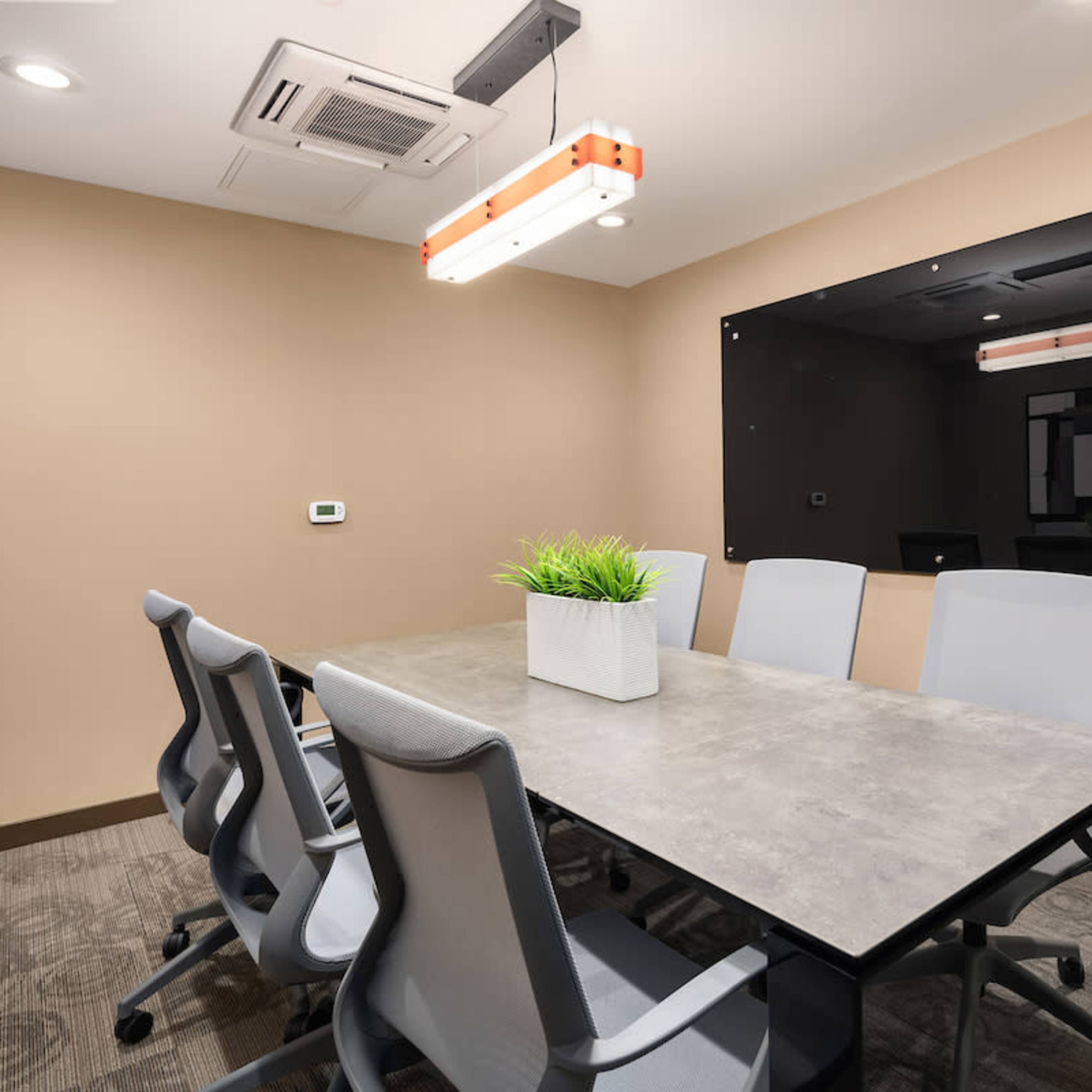 A modern conference room with a rectangular table surrounded by six gray chairs and a wall-mounted black board.