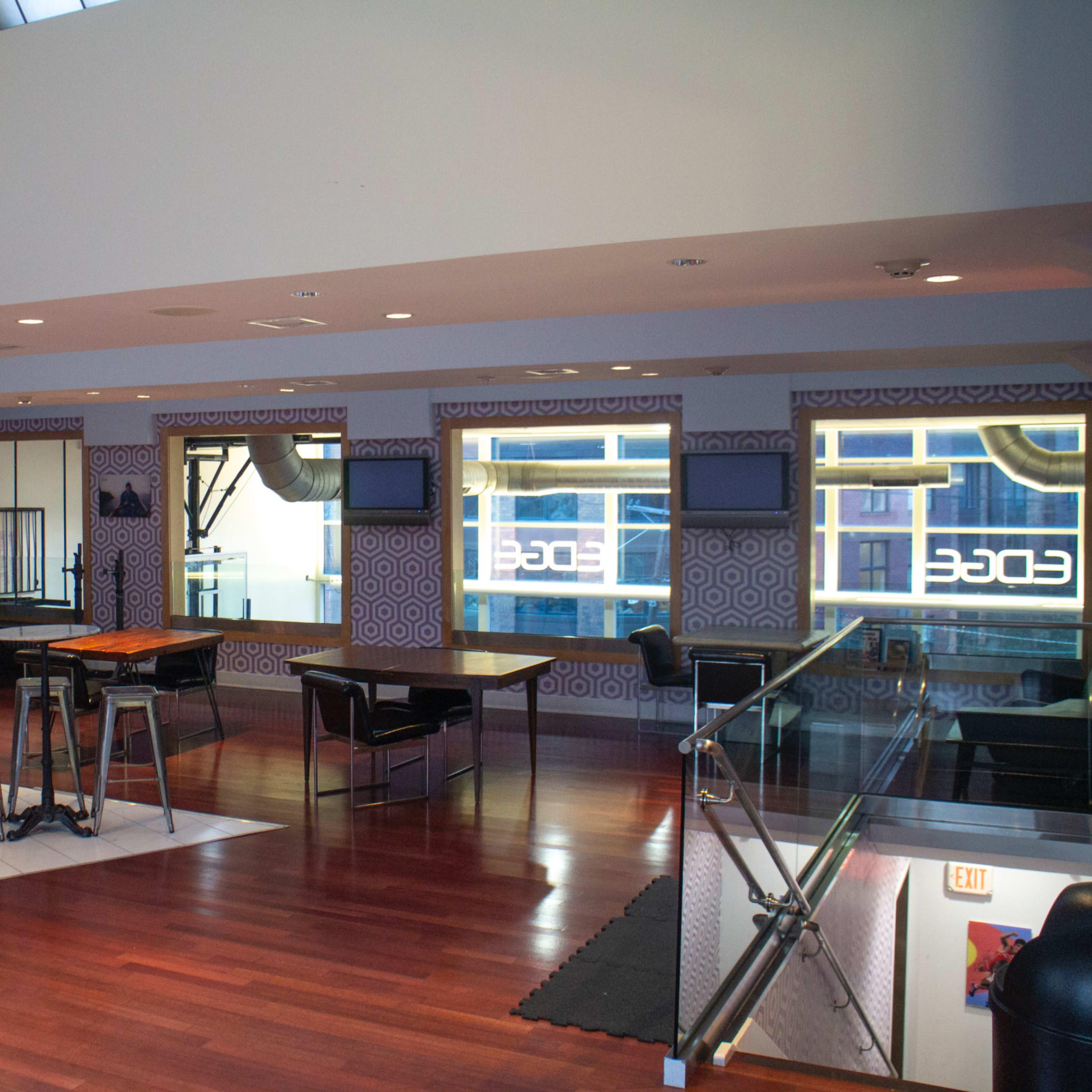 A modern interior space with hardwood flooring, seating areas, and patterned wallpaper, featuring a kitchen and multiple screens.