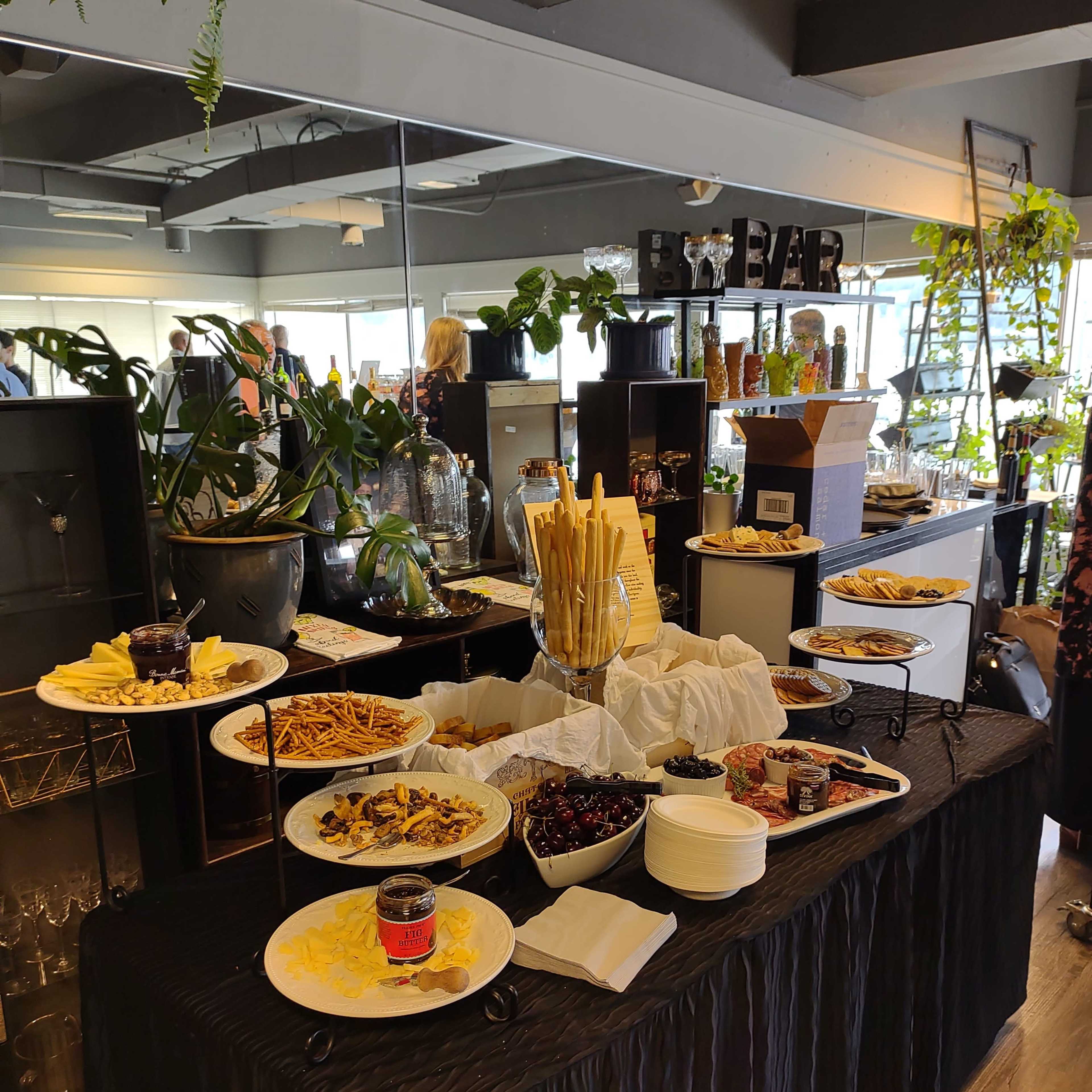 A buffet table is set with various appetizers and snacks, surrounded by indoor plants and decorative items.