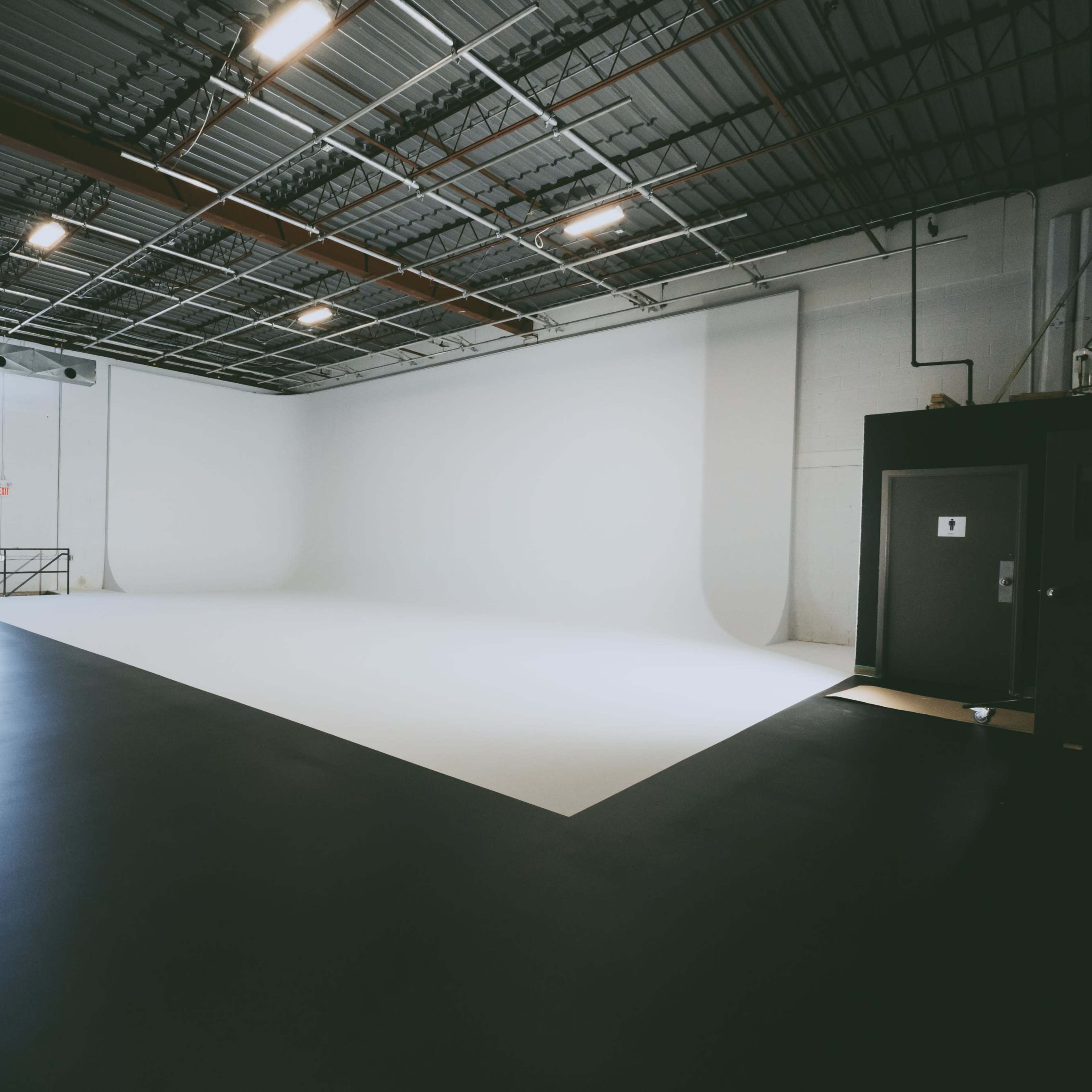 A spacious studio with a white seamless backdrop, concrete flooring, and overhead lighting.