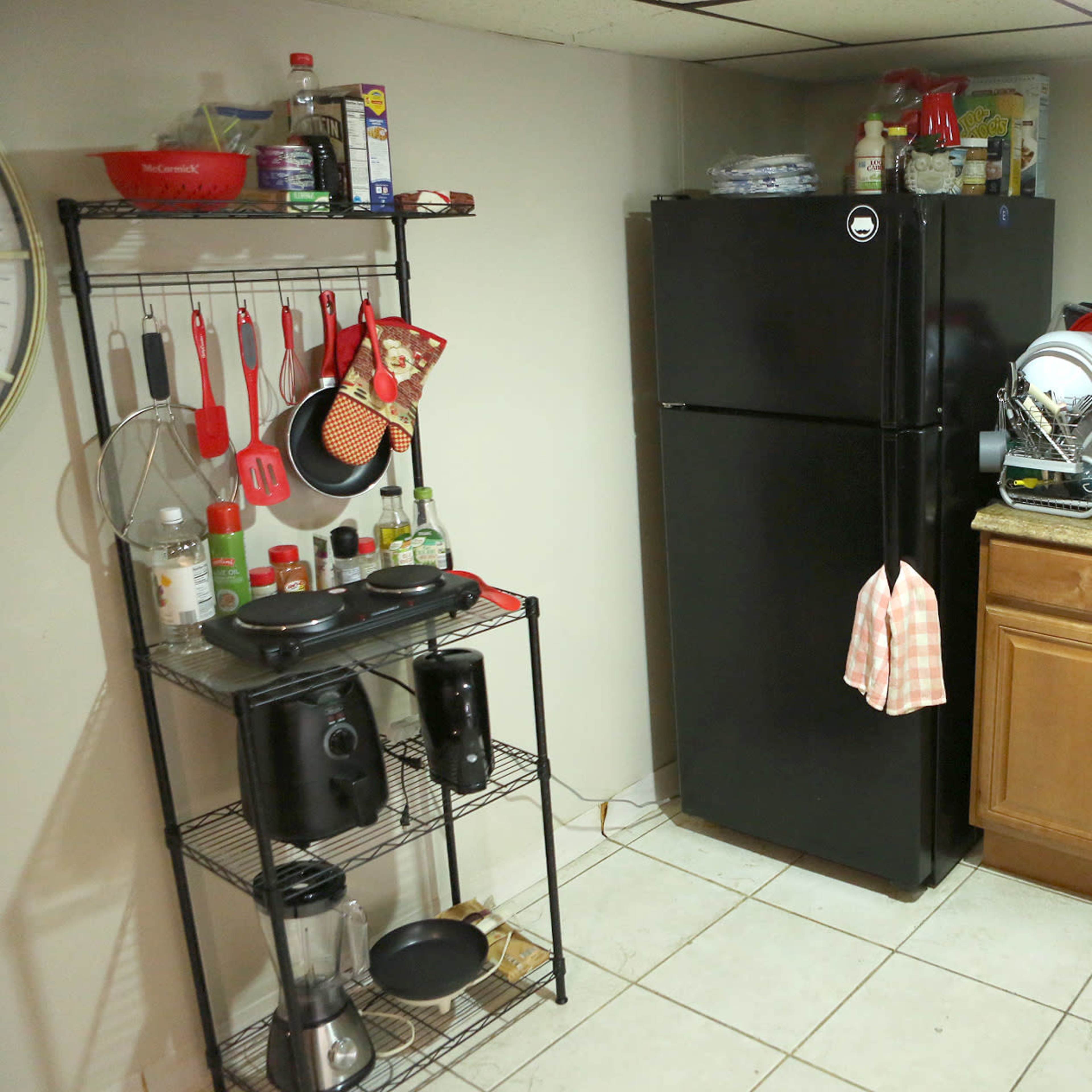 A small kitchen area with a black refrigerator, a microwave, and a sink surrounded by various kitchen utensils, appliances, and cabinets.