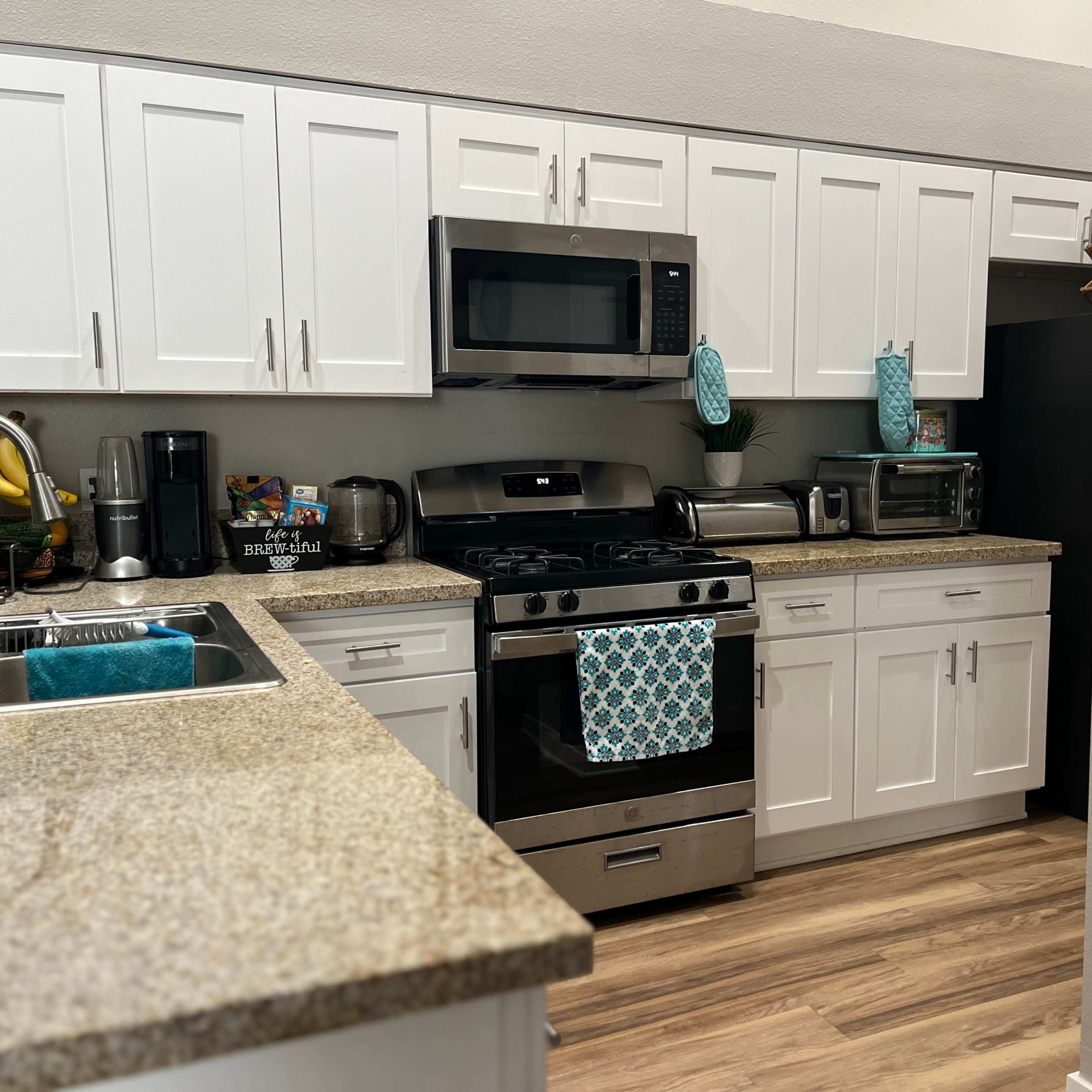 A modern kitchen with white cabinets, a granite countertop, stainless steel appliances, and a blue decorative towel hanging on the oven.