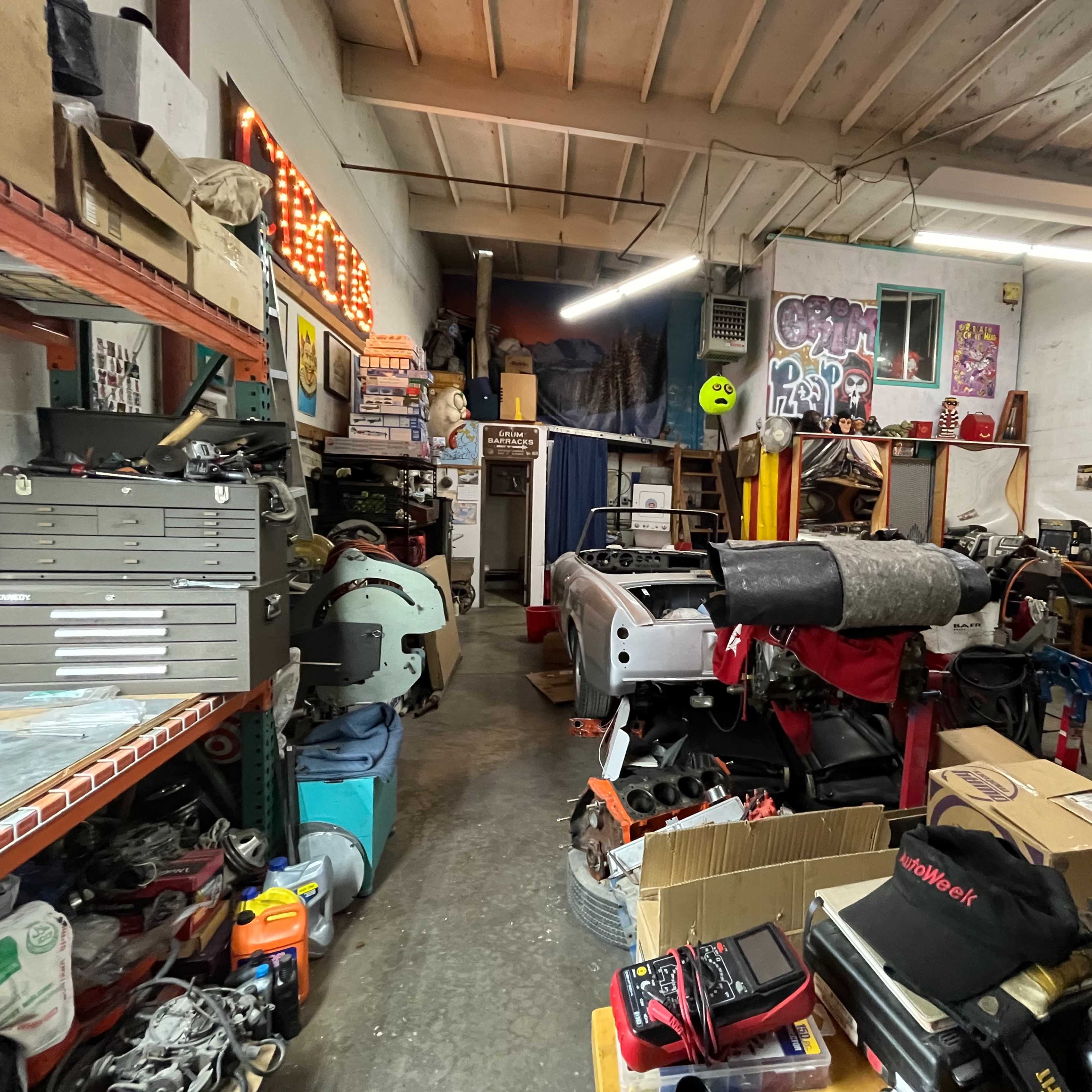 A cluttered garage workshop filled with various tools, equipment, and automotive parts.