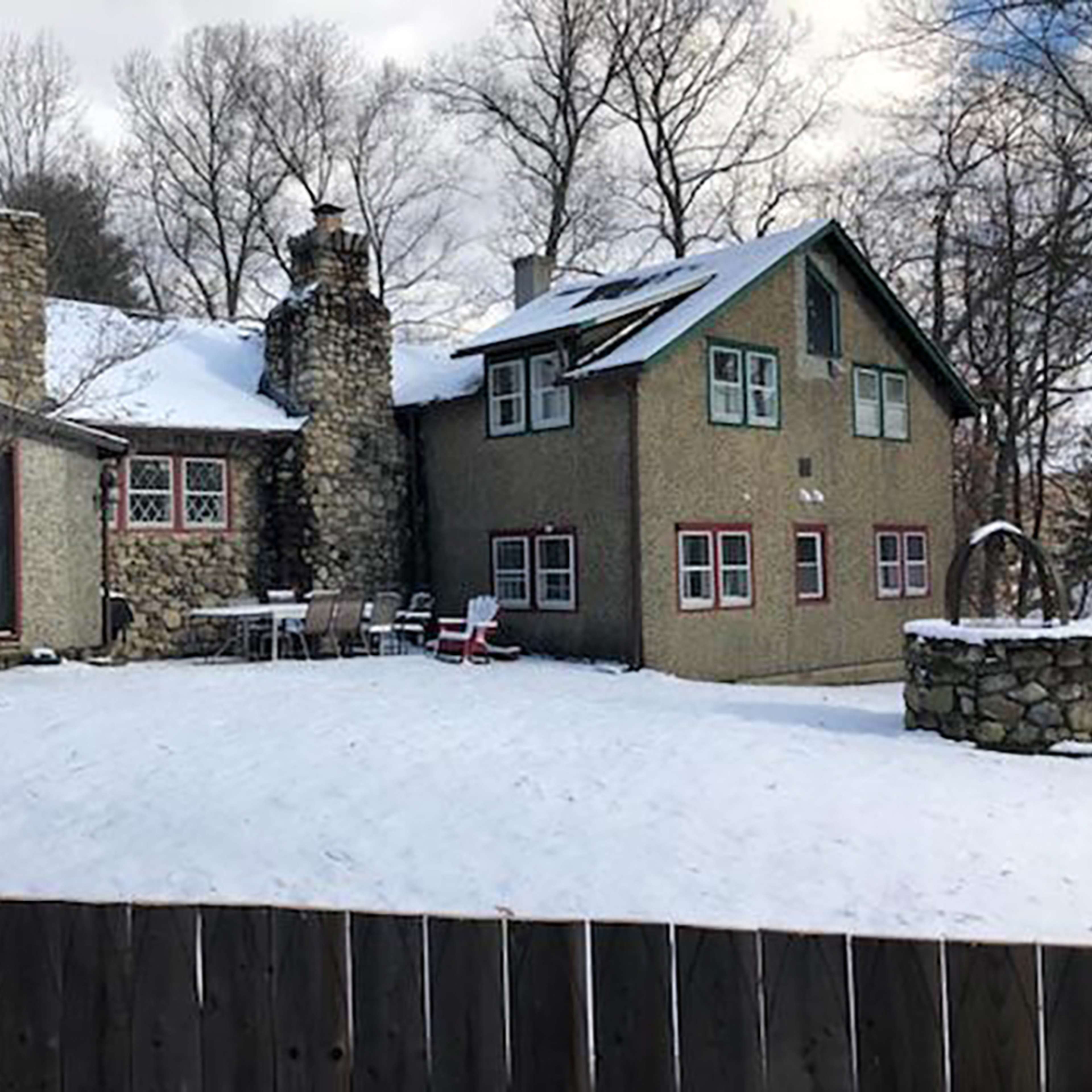 A stone and stucco house with a chimney and a fenced yard covered in snow.