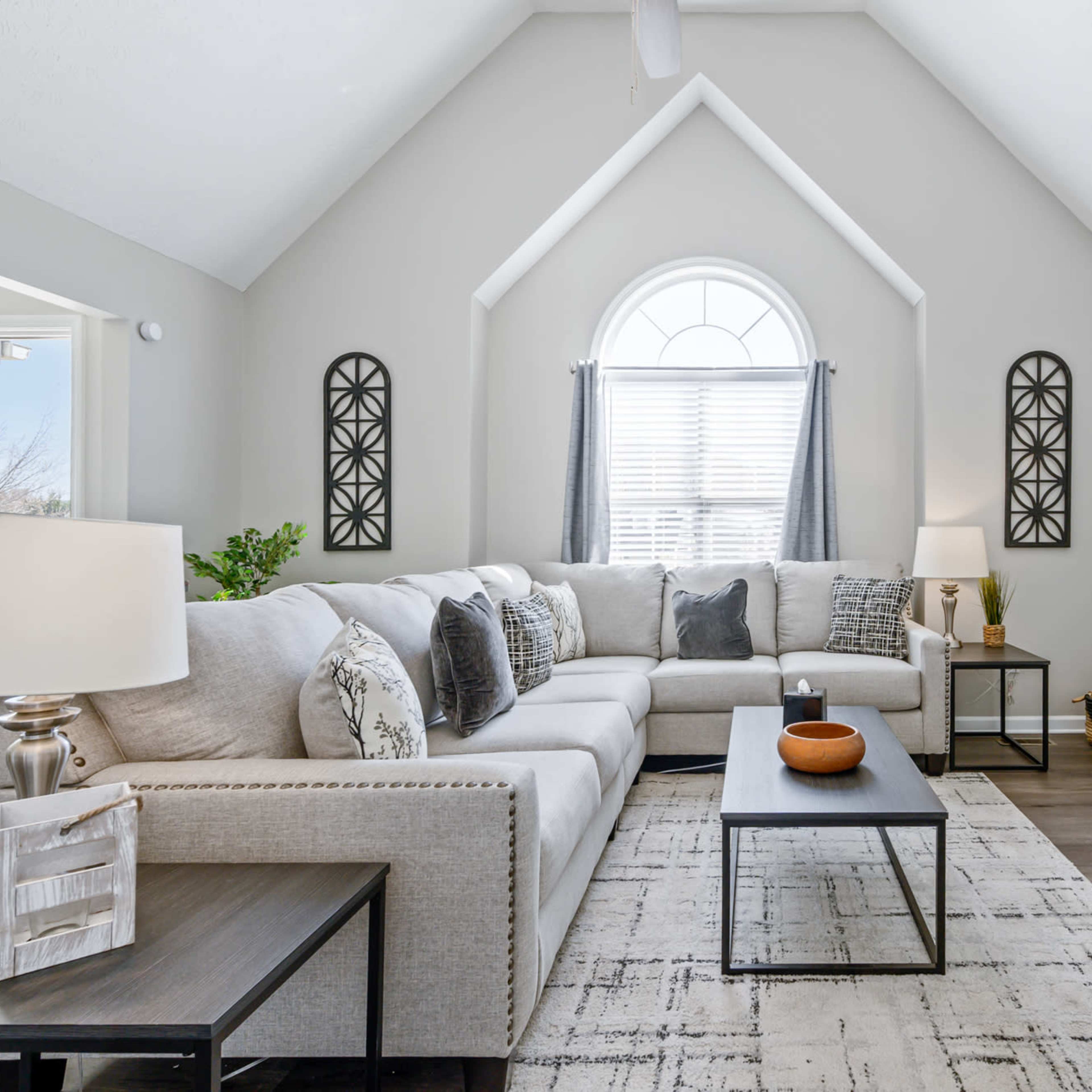 The living room features a large sectional sofa, a coffee table, and large windows with natural light, creating an open and inviting atmosphere.
