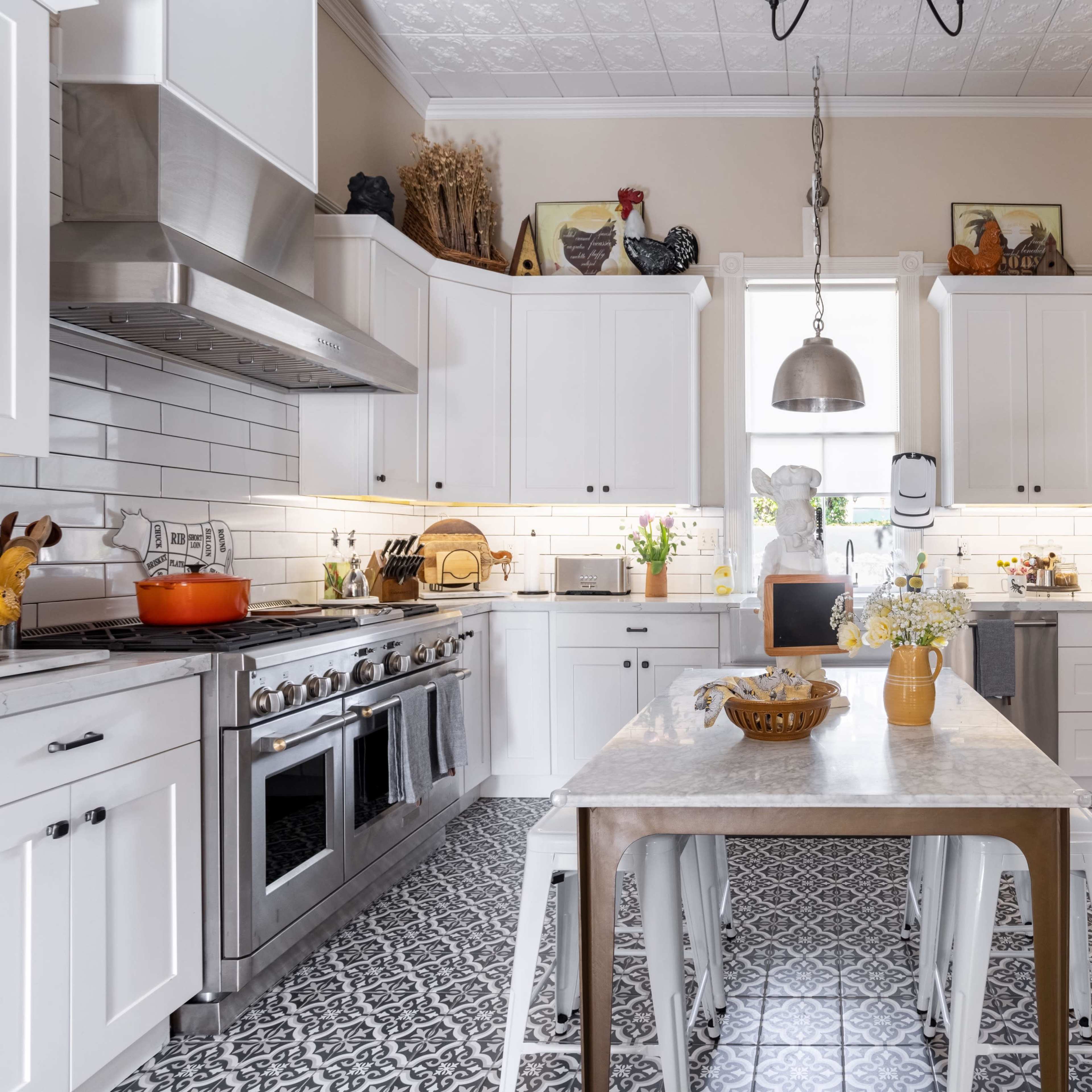 A modern kitchen features white cabinetry, stainless steel appliances, a central island with a marble top, and decorative tile flooring.
