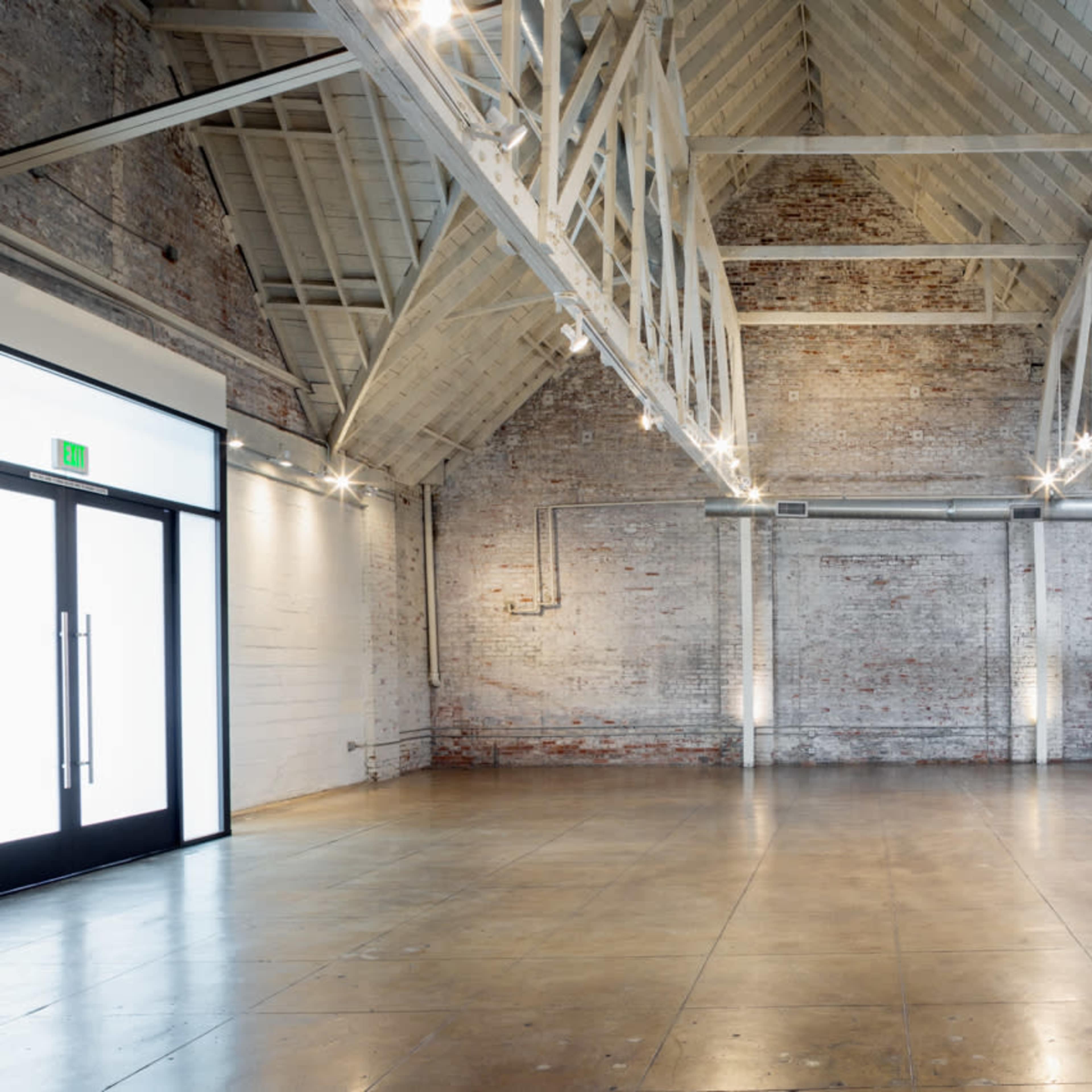 A spacious, industrial-style interior with exposed brick walls, high ceilings, and polished concrete flooring.