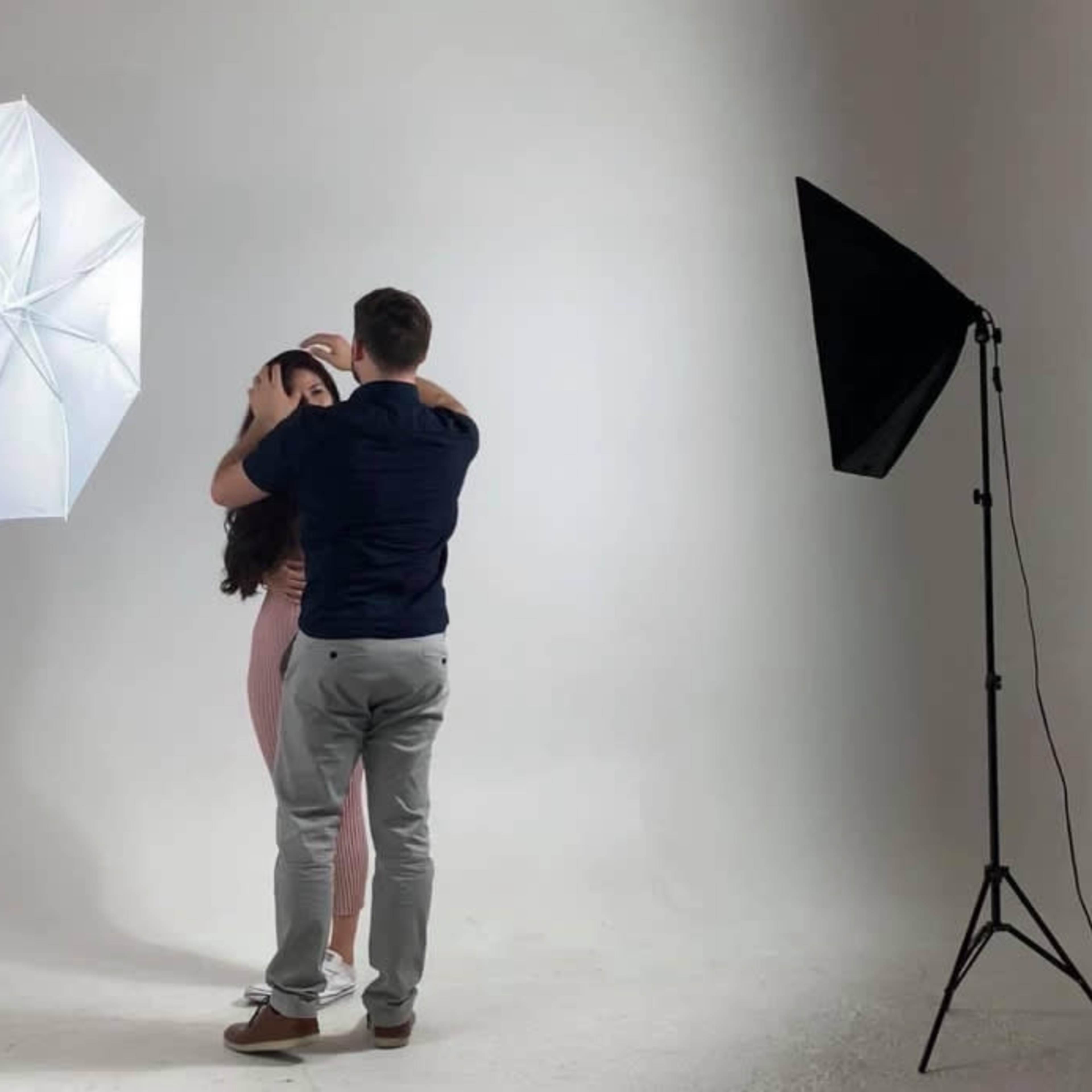 A man and a woman are posing closely together in a photography studio with softbox lights on either side.
