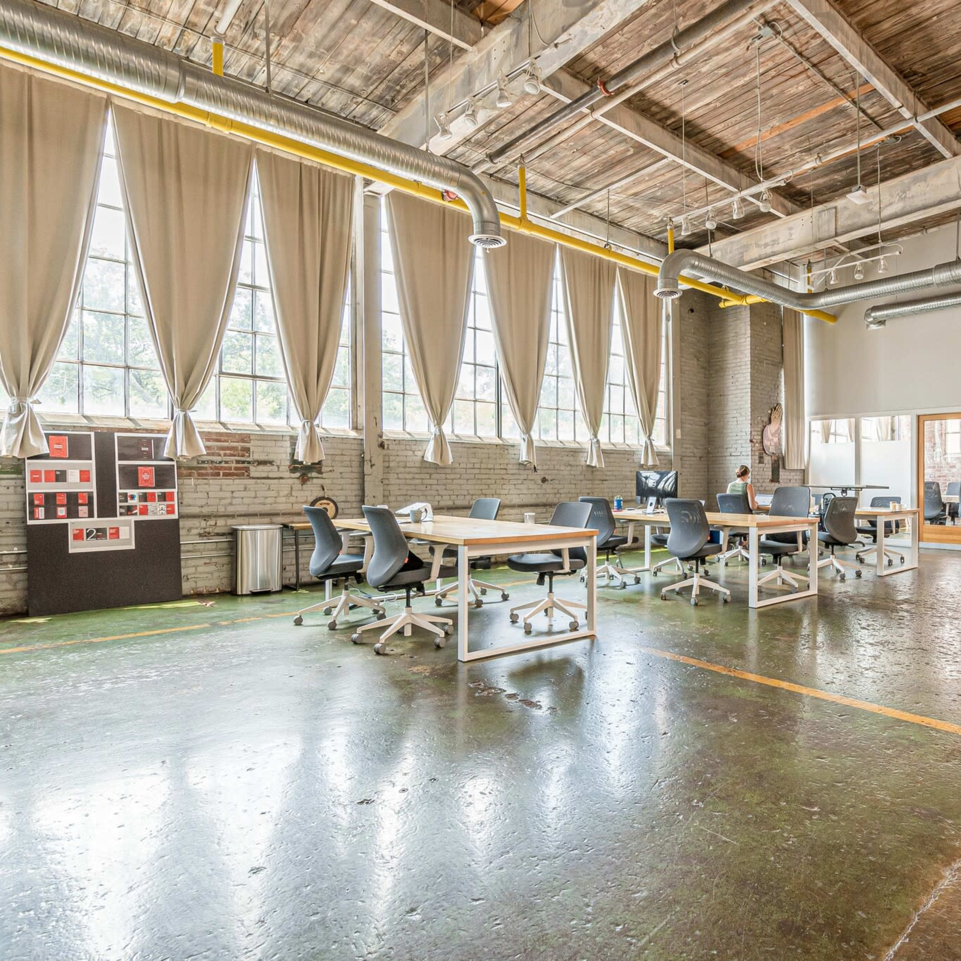 A spacious, modern office with large windows, several workstations, and a meeting area with glass walls.