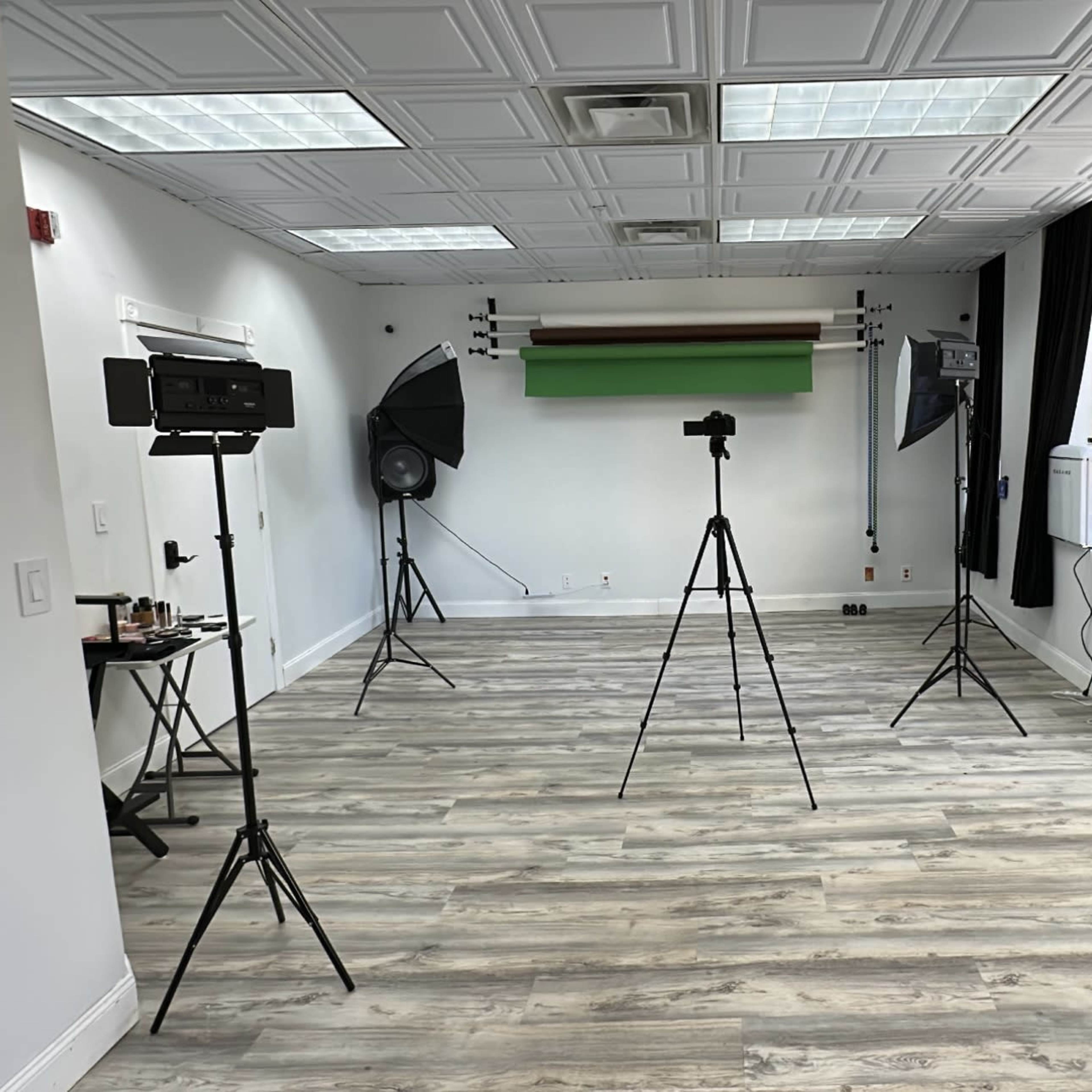 A photography studio with tripods, lighting equipment, and a green backdrop set up in a spacious room.