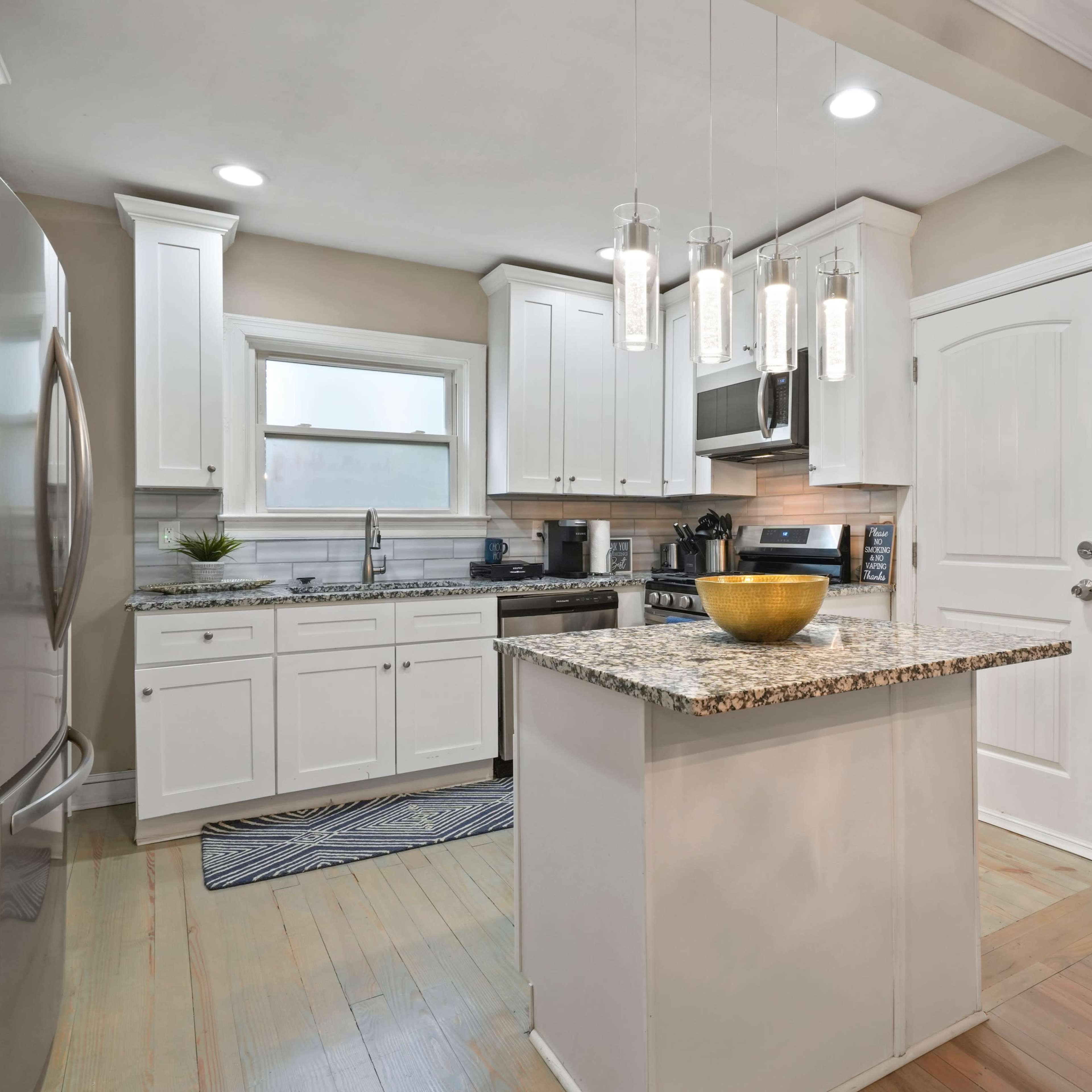 A modern kitchen features white cabinetry, granite countertops, stainless steel appliances, and pendant lighting over an island.