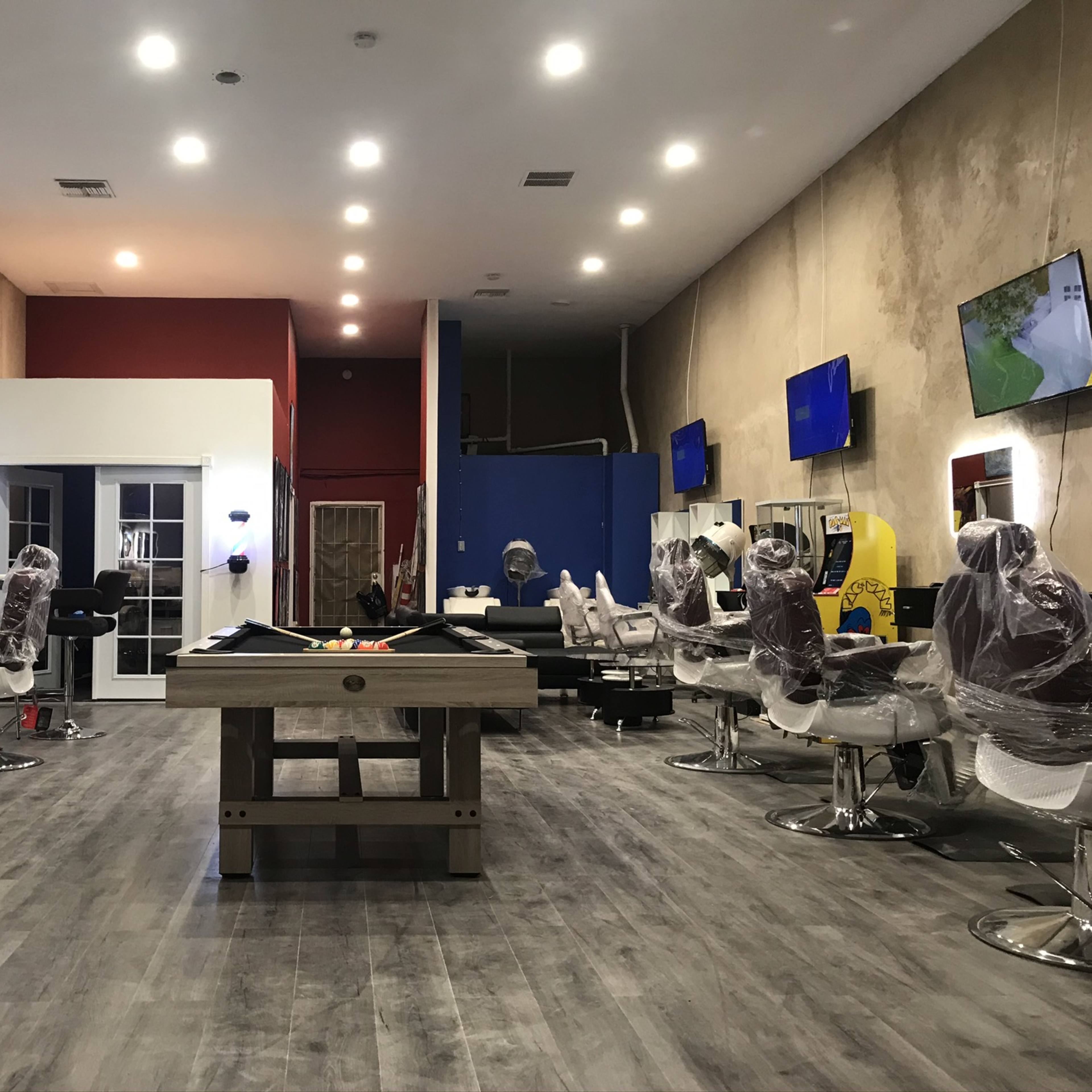An empty hair salon with several styling stations, each covered with plastic, and two large televisions mounted on the walls.
