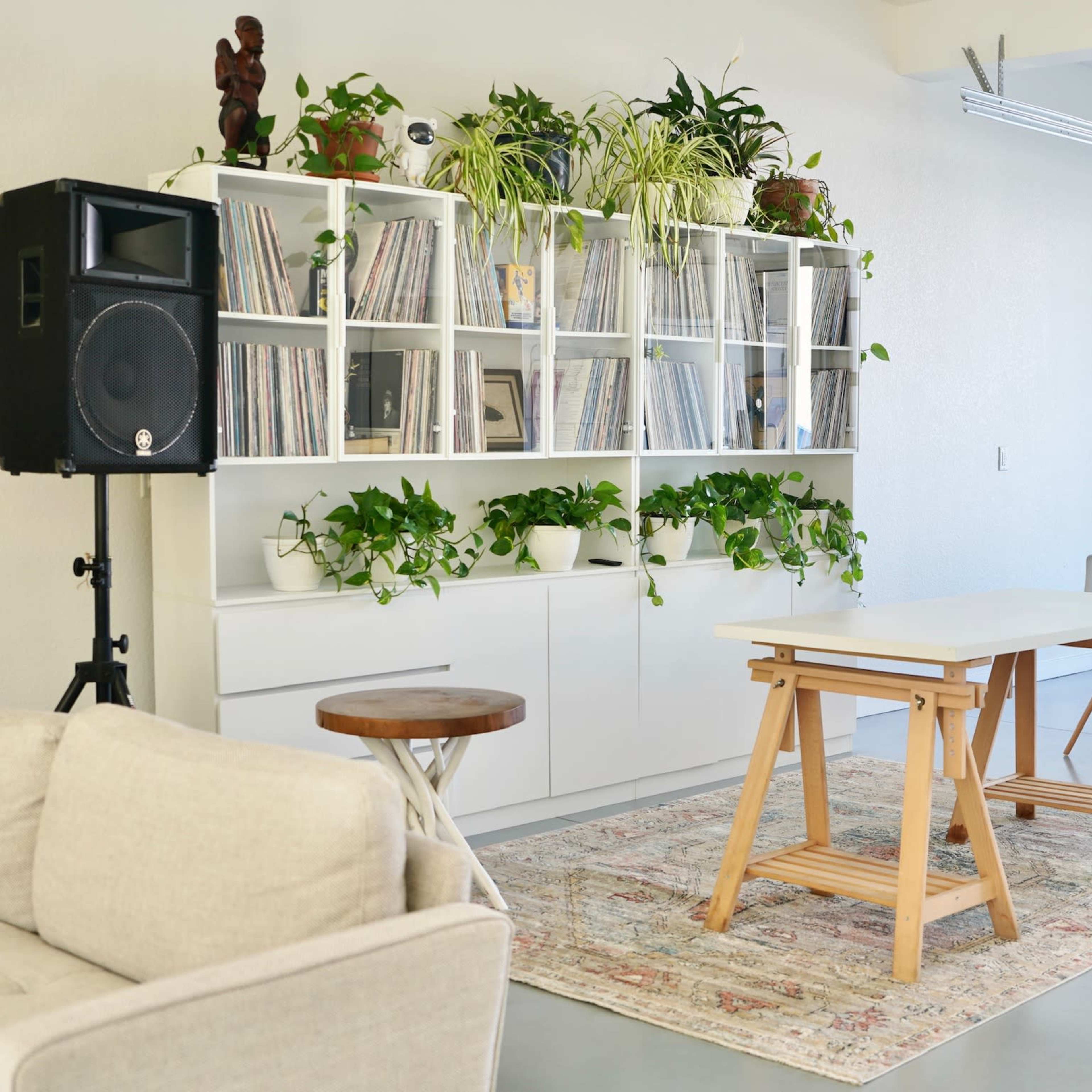 A modern, open space features a shelving unit filled with vinyl records, a large dining table, and a seating area with a light-colored sofa.