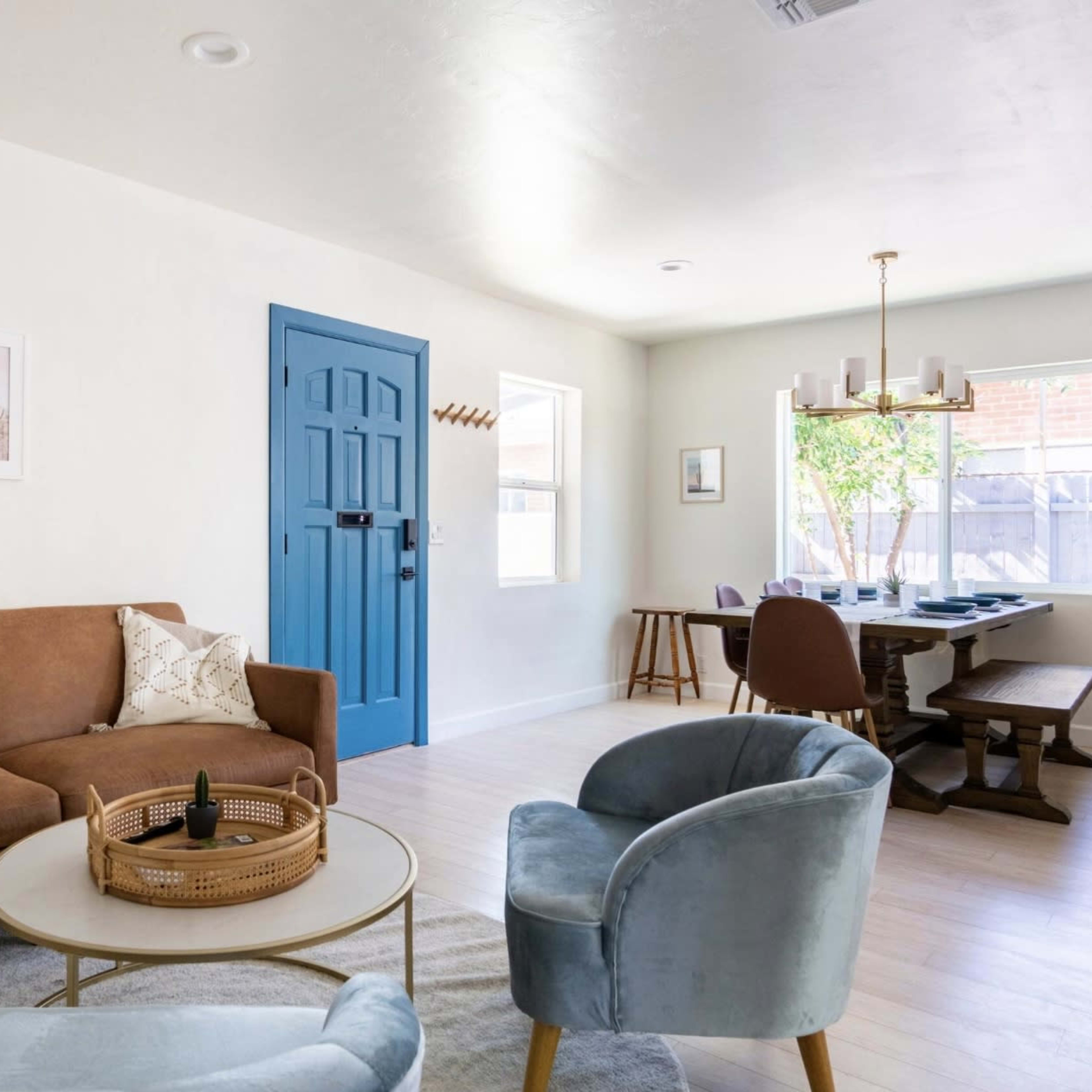 A living room features a brown couch, a blue door, and a dining table set against white walls.