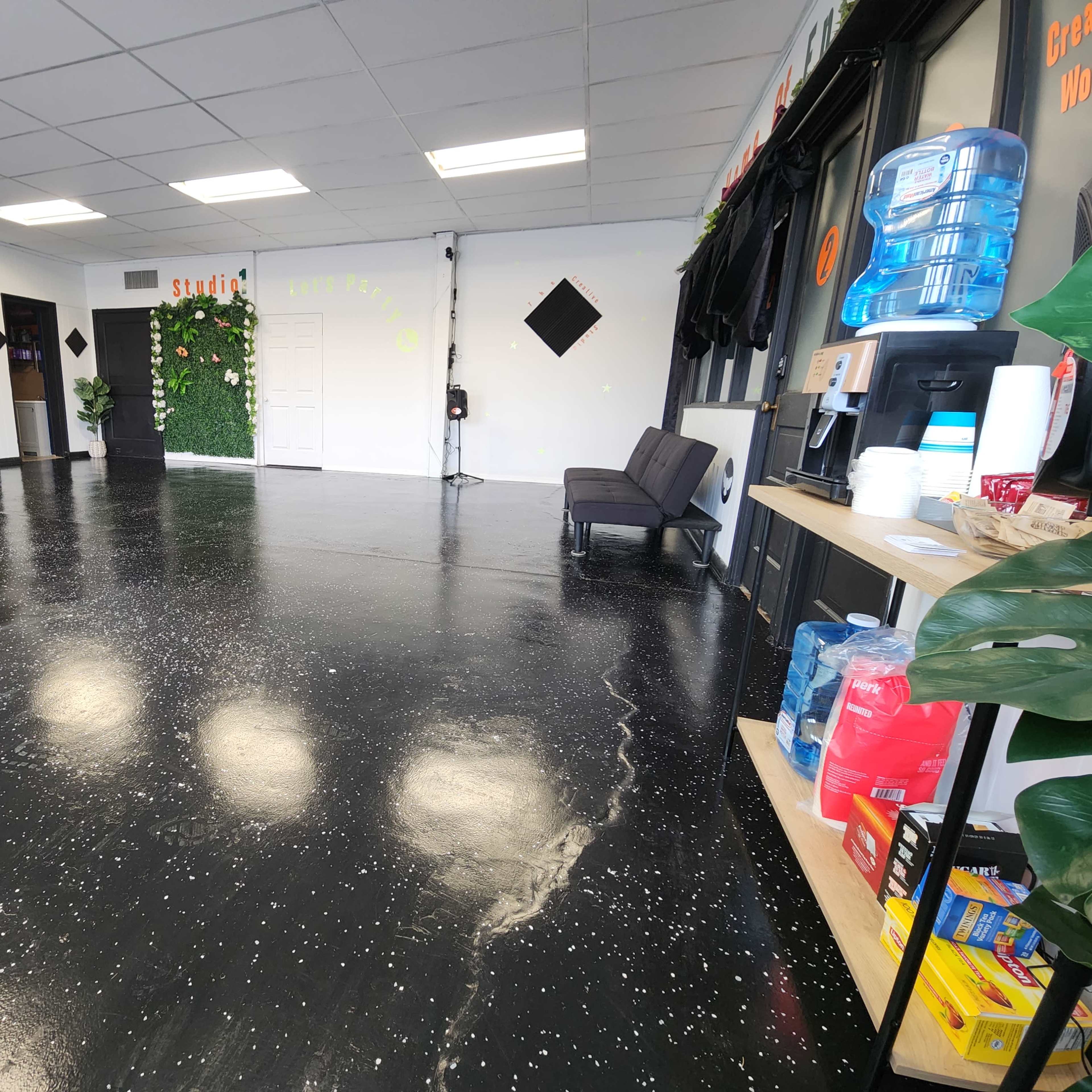 An empty room with a polished black floor, a few plants on the walls, and a beverage station on the right side.
