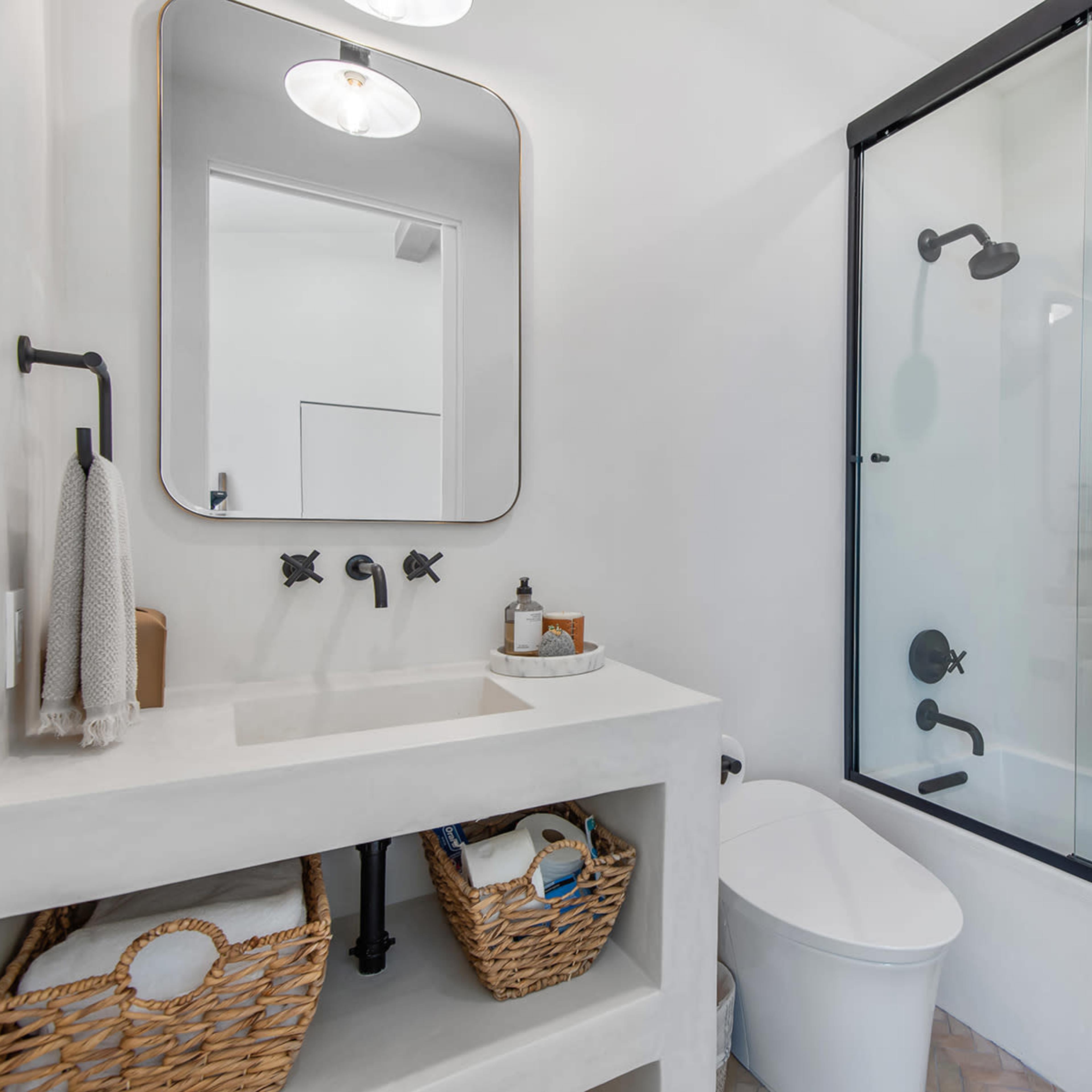 A modern bathroom featuring a glass shower, a white sink with decorative baskets underneath, and neatly hung towels.