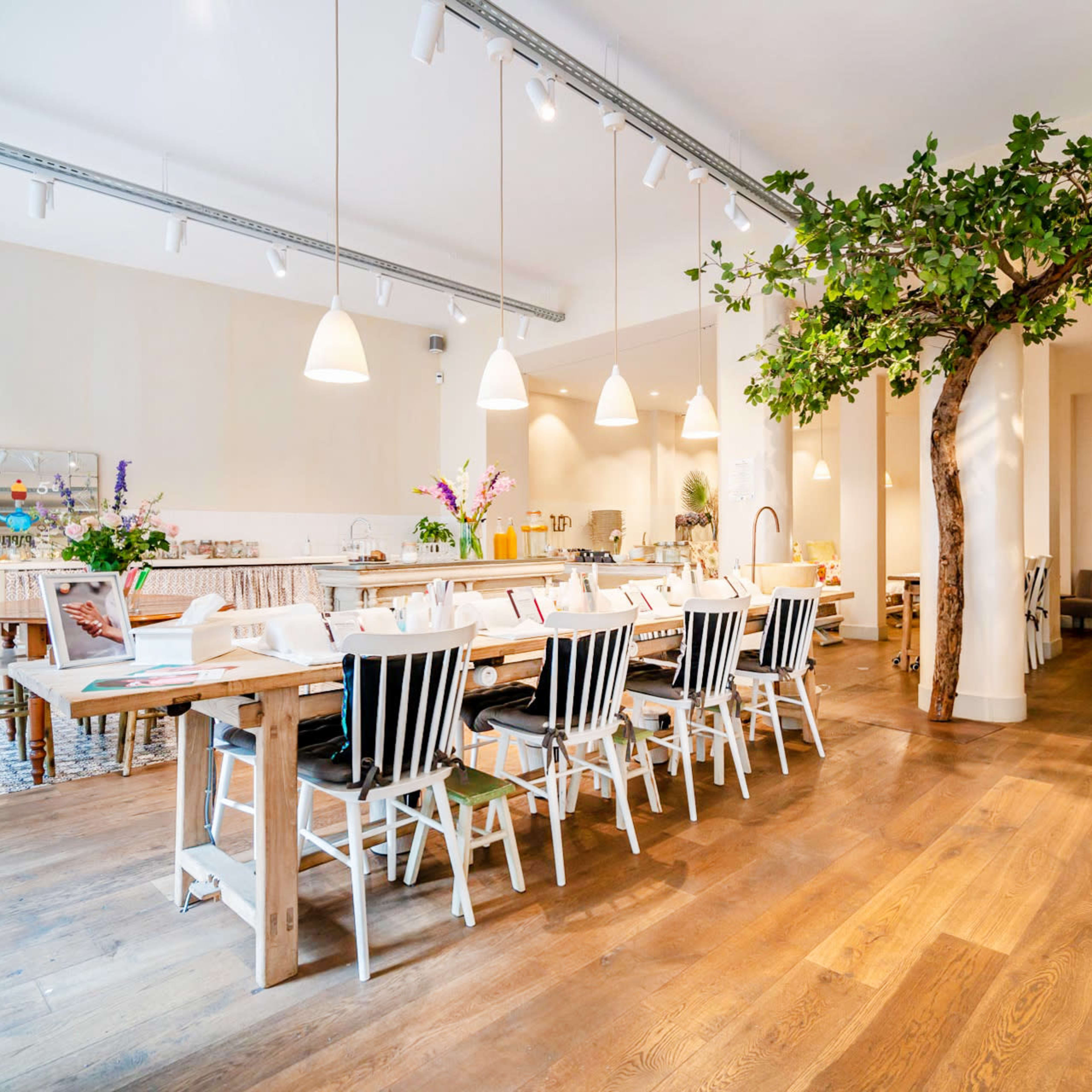 A spacious, modern dining area with a long wooden table surrounded by black-and-white striped chairs, and a decorative tree in the corner.