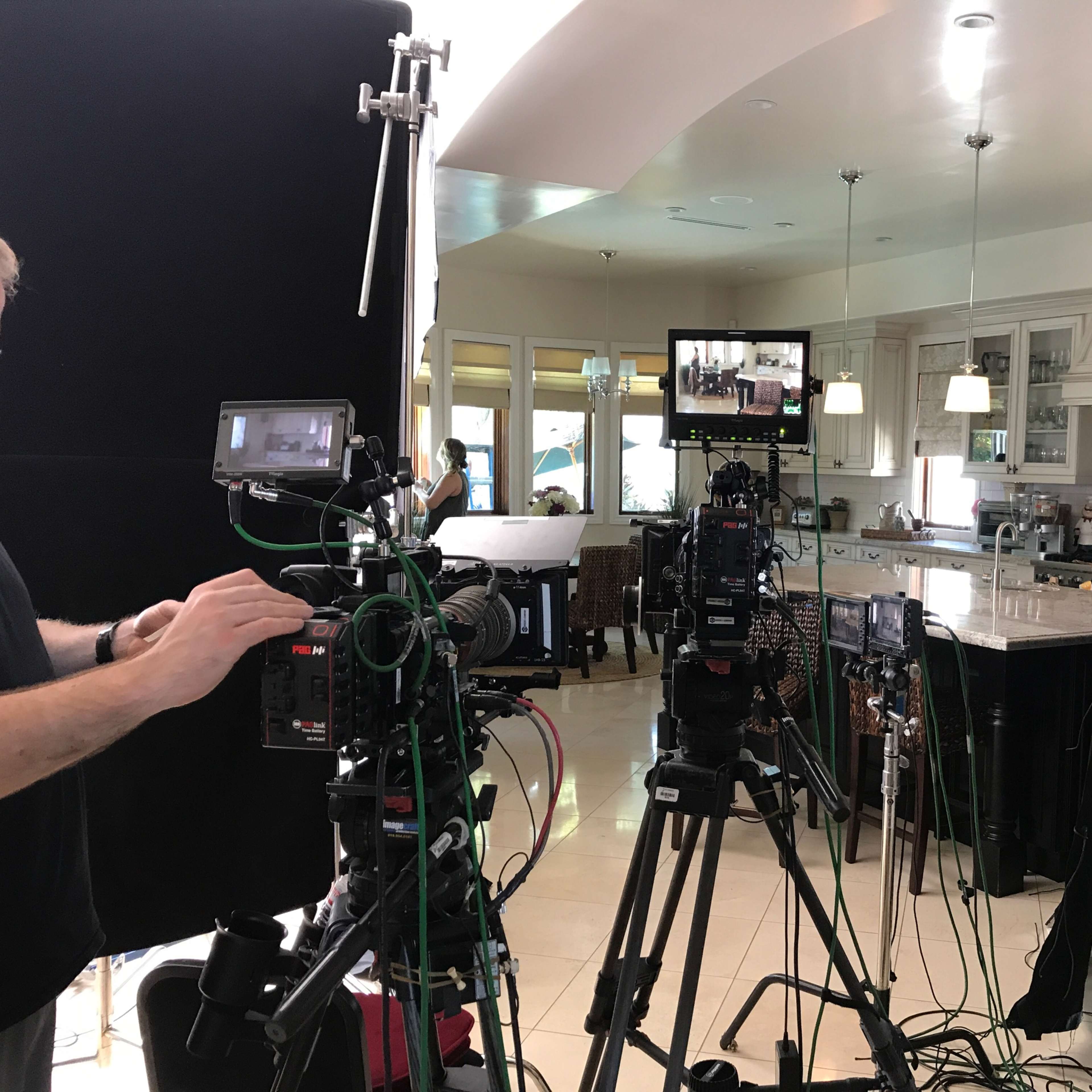 A film crew sets up cameras and equipment in a well-lit kitchen for a shooting scene.
