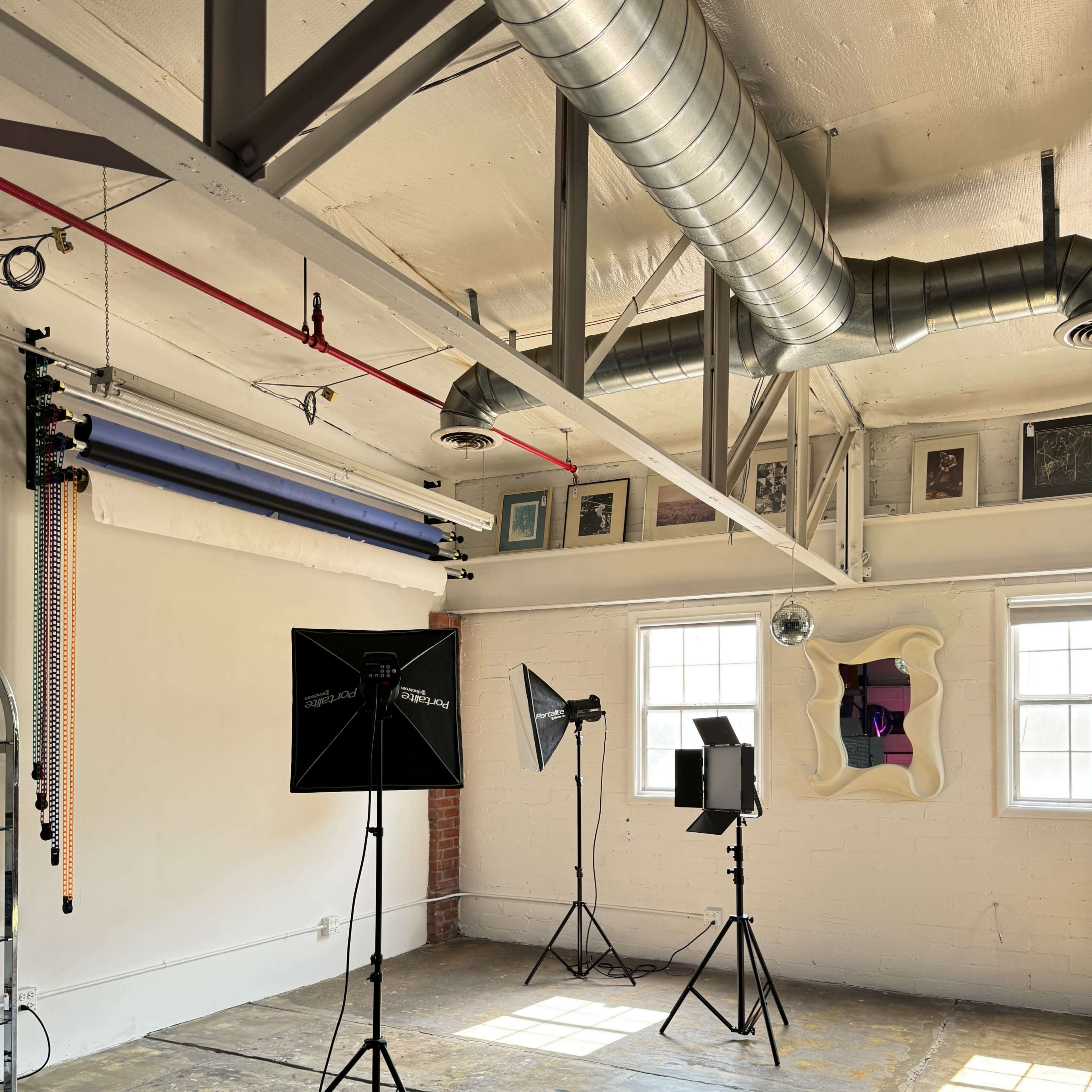 A photo studio equipped with three lighting setups, a backdrop hanging system, and an abstract wall decoration.