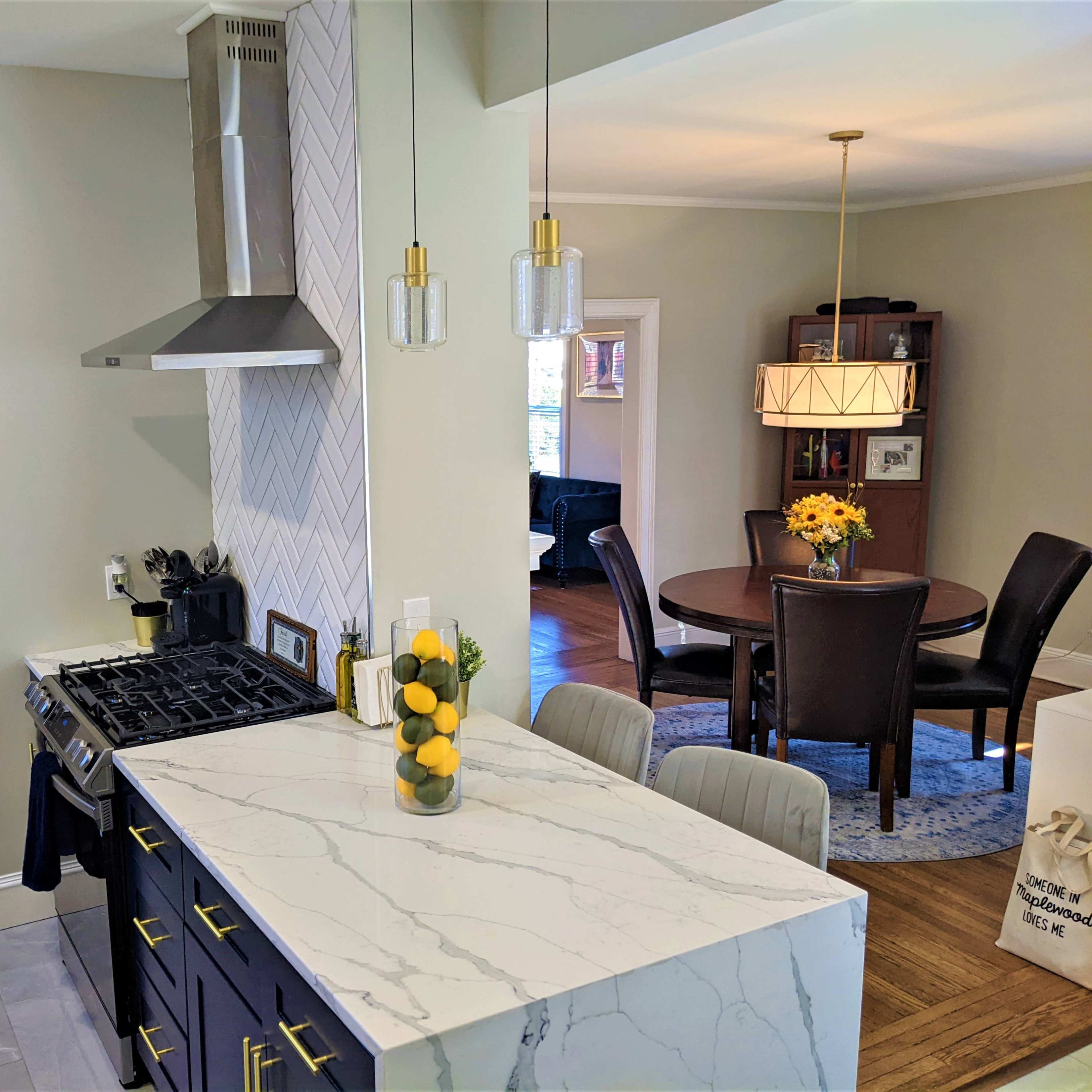 A modern kitchen with a gas stovetop, a marble countertop adorned with lemons, and a dining area visible in the background.